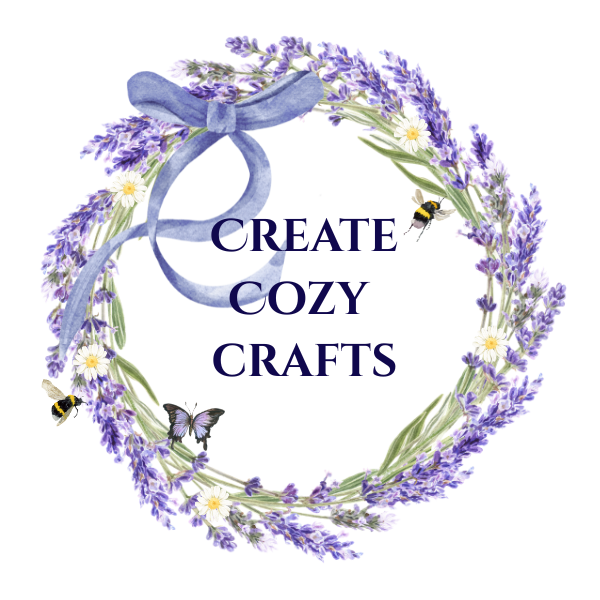 A decorative wreath made of lavender flowers and white daisies with a blue ribbon at the top, surrounding the text 'Create Cozy Crafts' with small bees and a butterfly around the wreath.
