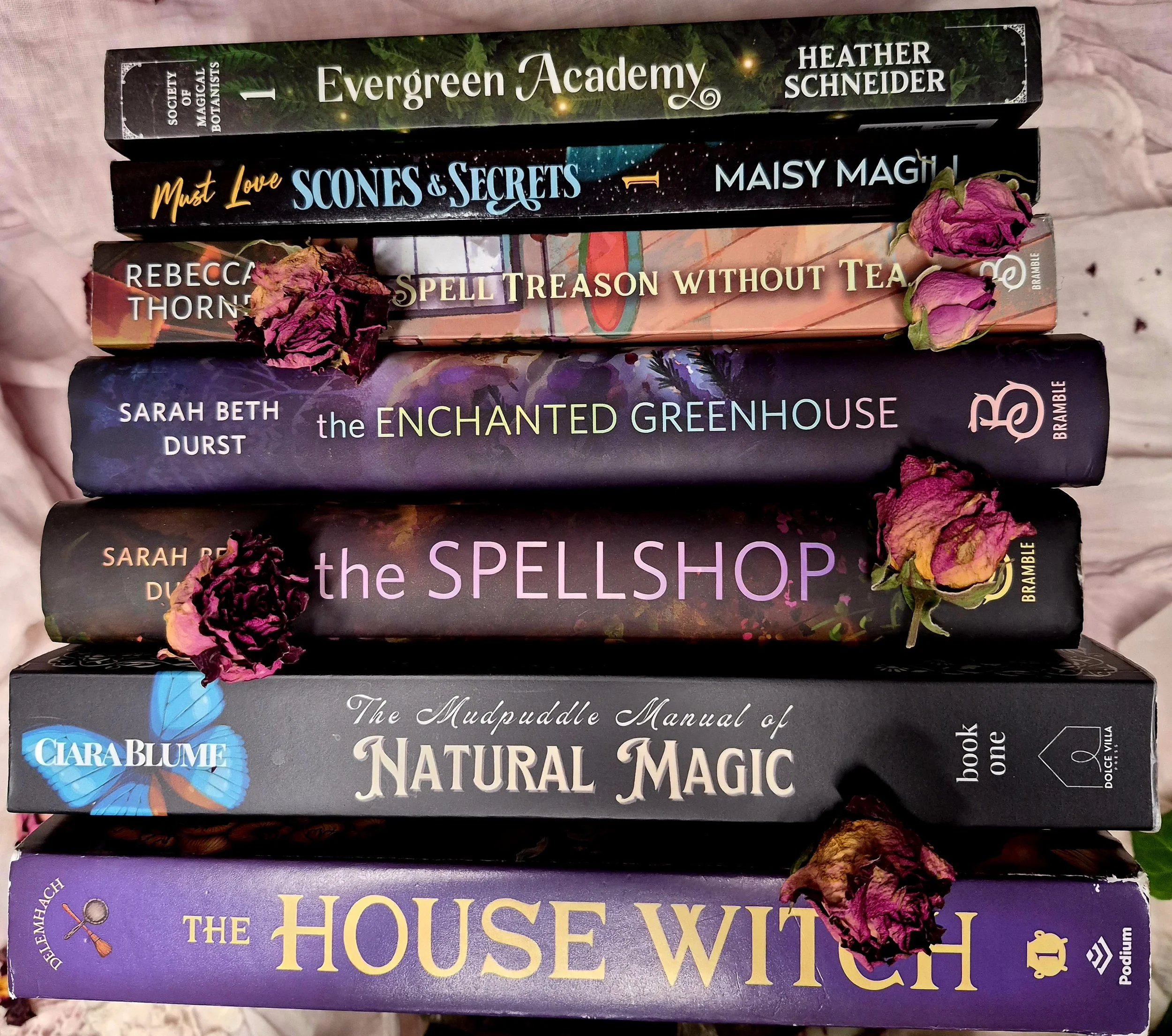 Stack of eight books with dried pink flowers on them, arranged against a pink background.