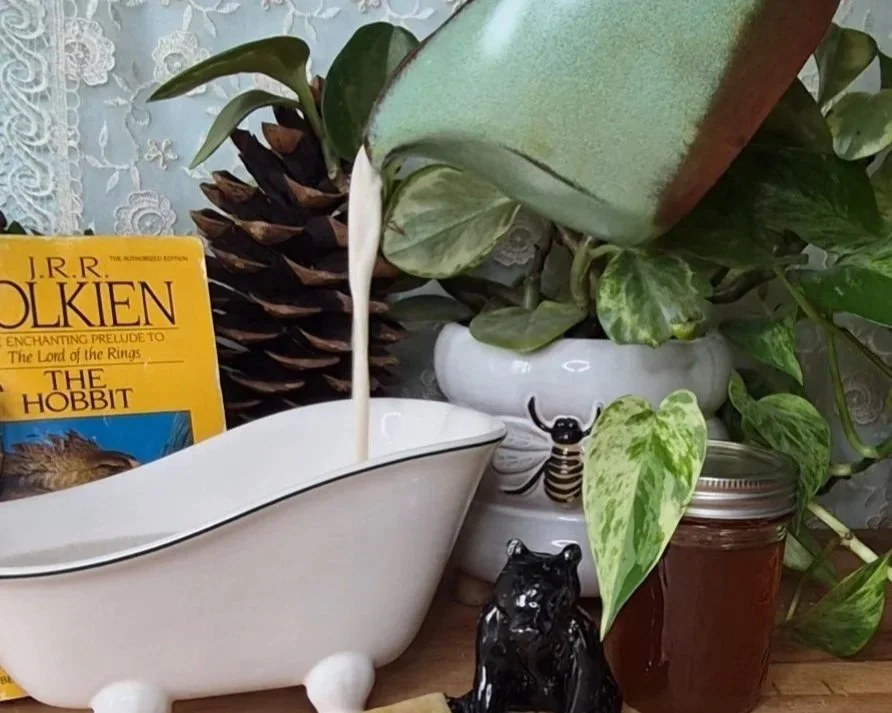 creamy milk and honey herbal infused bath being poured into a tiny bathtub with The Hobbit book in the background