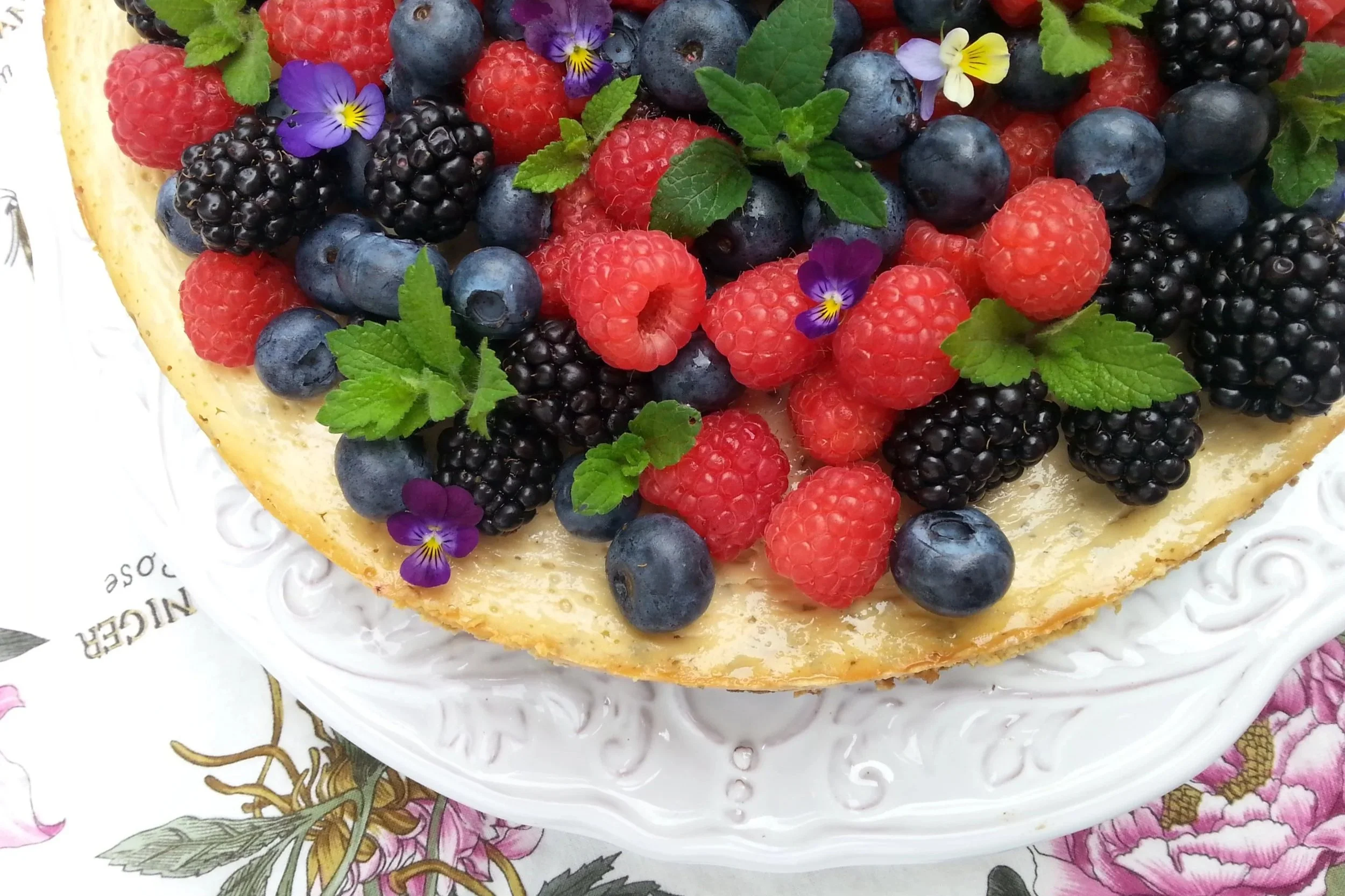cheesecake topped with berries, lemon balm sprigs, and pansies