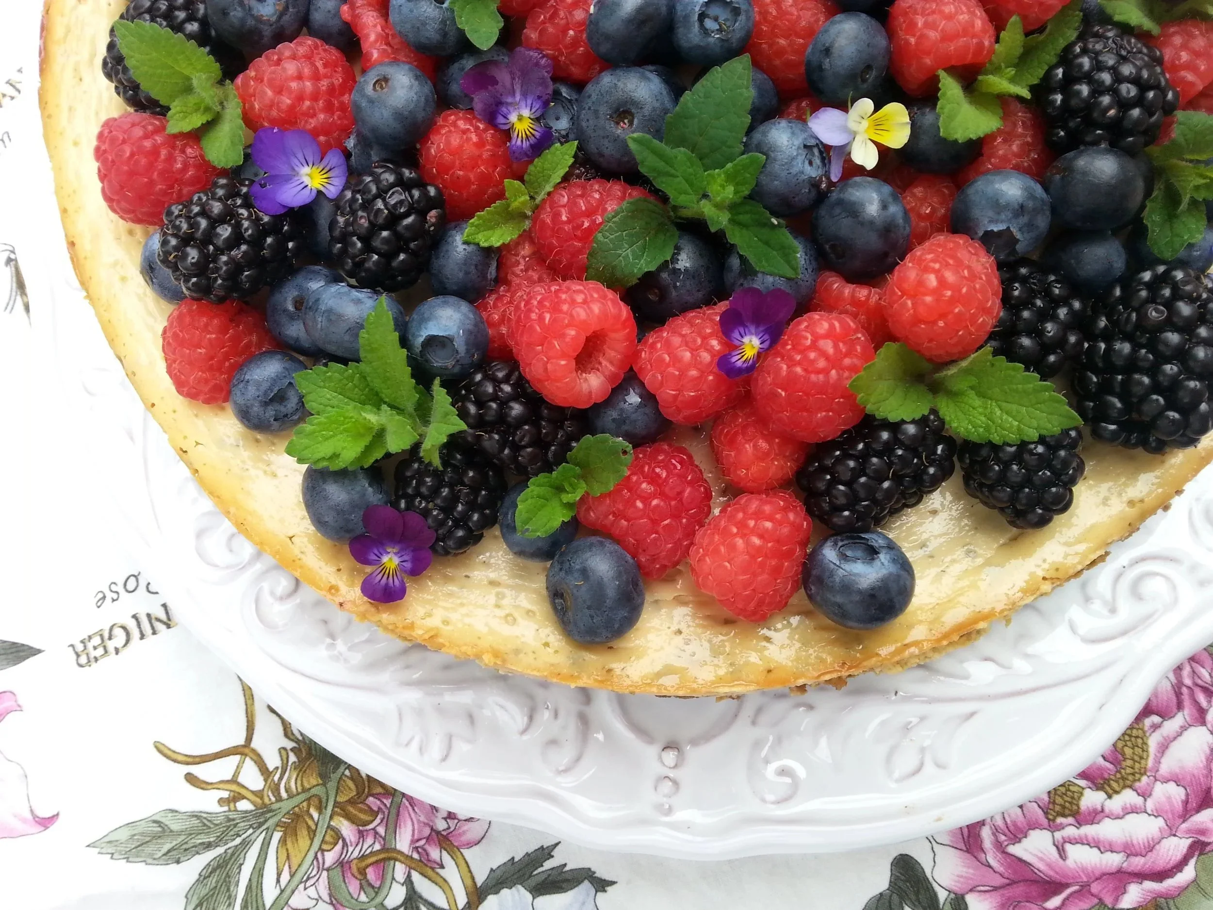 a picture of berries, fresh lemon balm, and pansies on top of cheesecake