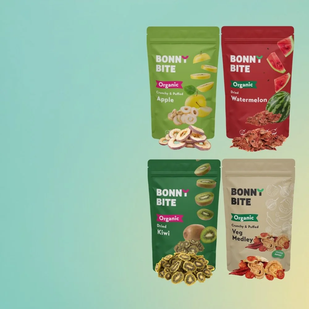 Four different packages of Bonny Bite organic crunchy and puffed snack mixes in green, red, and beige packaging. The green package contains apple flavored snacks, the red package watermelon flavored snacks, the green package kiwi flavored snacks, and the beige package vegetable medley flavored snacks. Each package has images of the respective fruits or vegetables depicted.