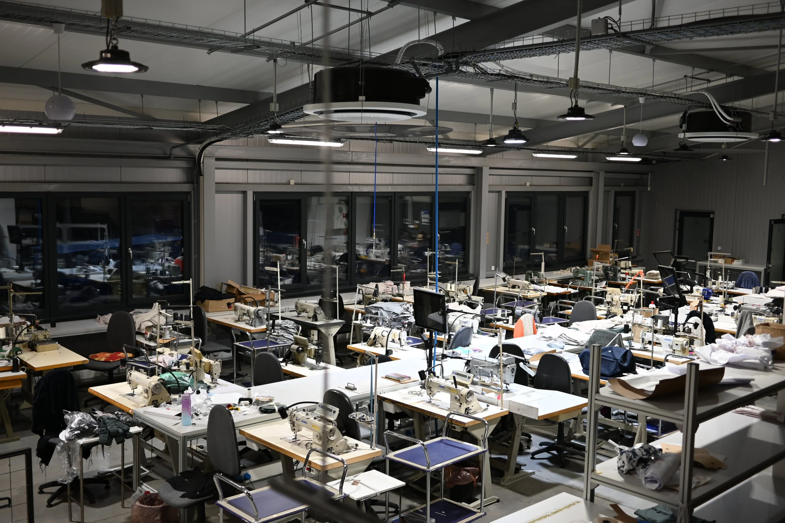 Moderná výrobná hala s veľkými oknami a prirodzeným svetlom. Tablety pripevnené na pracovné stanice šijacích strojov umožňujú lepšie organizovať prácu a pomocou videí školiť jednoduché pracovné úkony. Špeciálne valy klimatizácie pripevnené na strope 