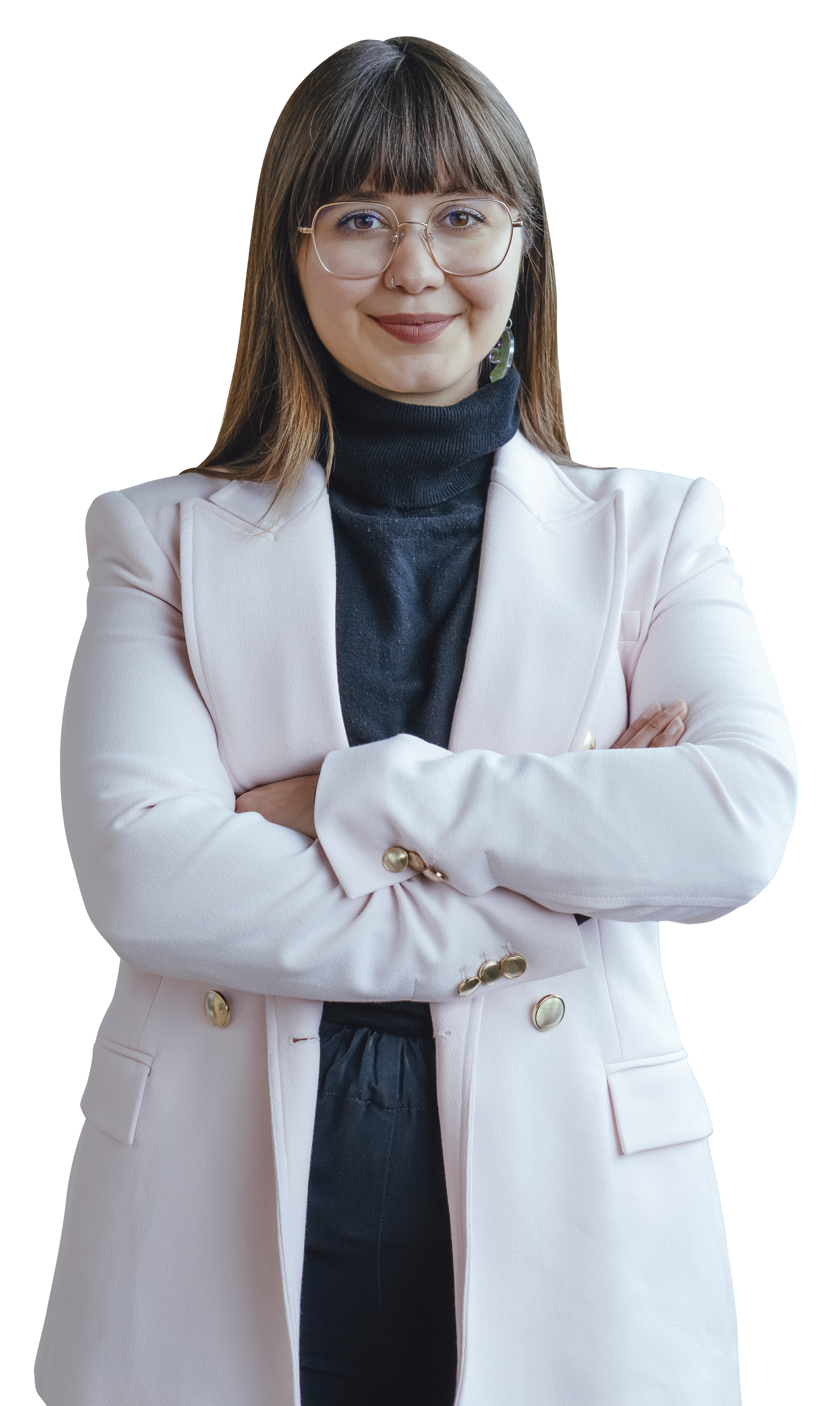 A woman wearing glasses, a light pink blazer with gold buttons, a black turtleneck, and black pants, standing with arms crossed and smiling.