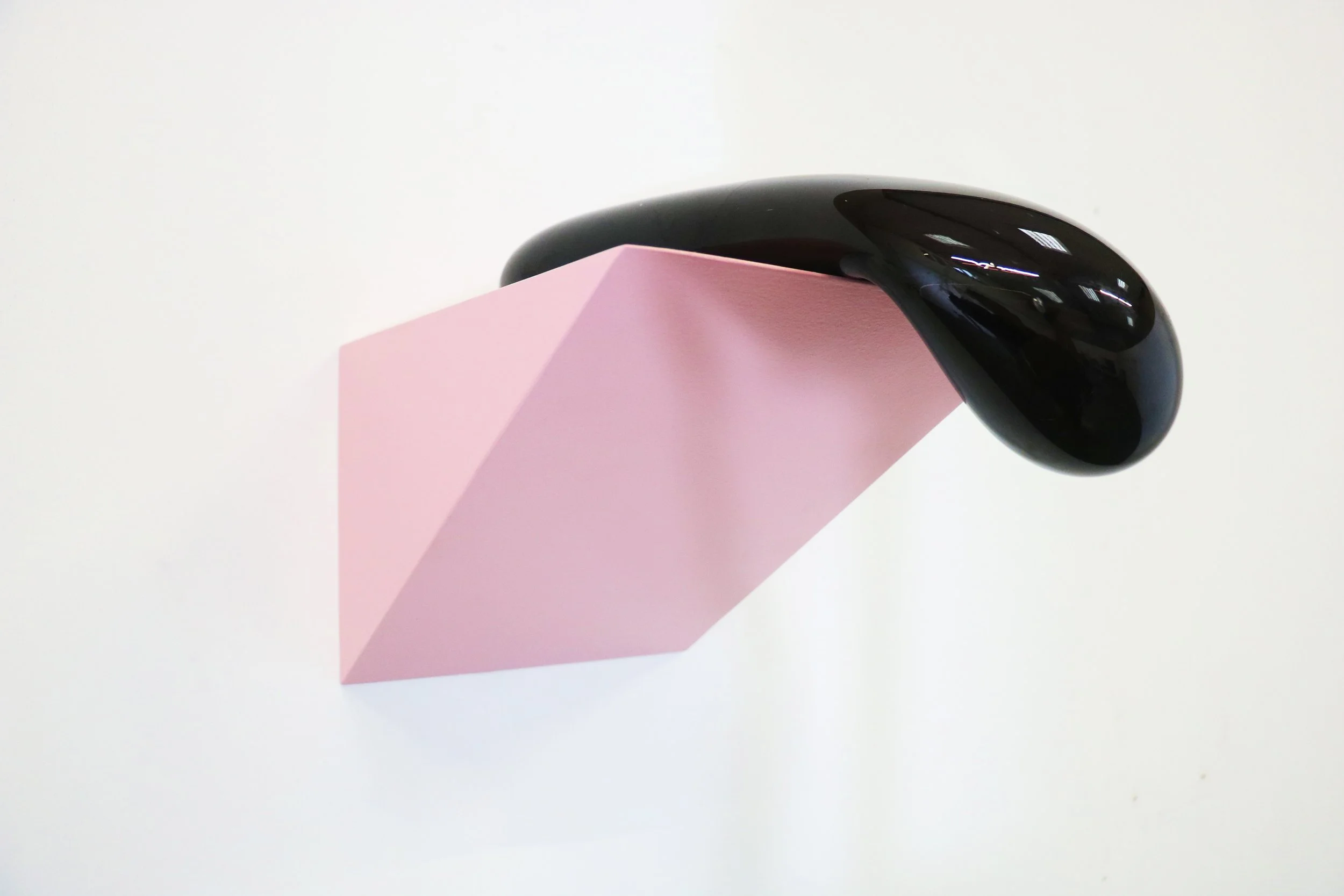 Close-up of a pink paper cube with a shiny black computer mouse on top, against a plain white background.
