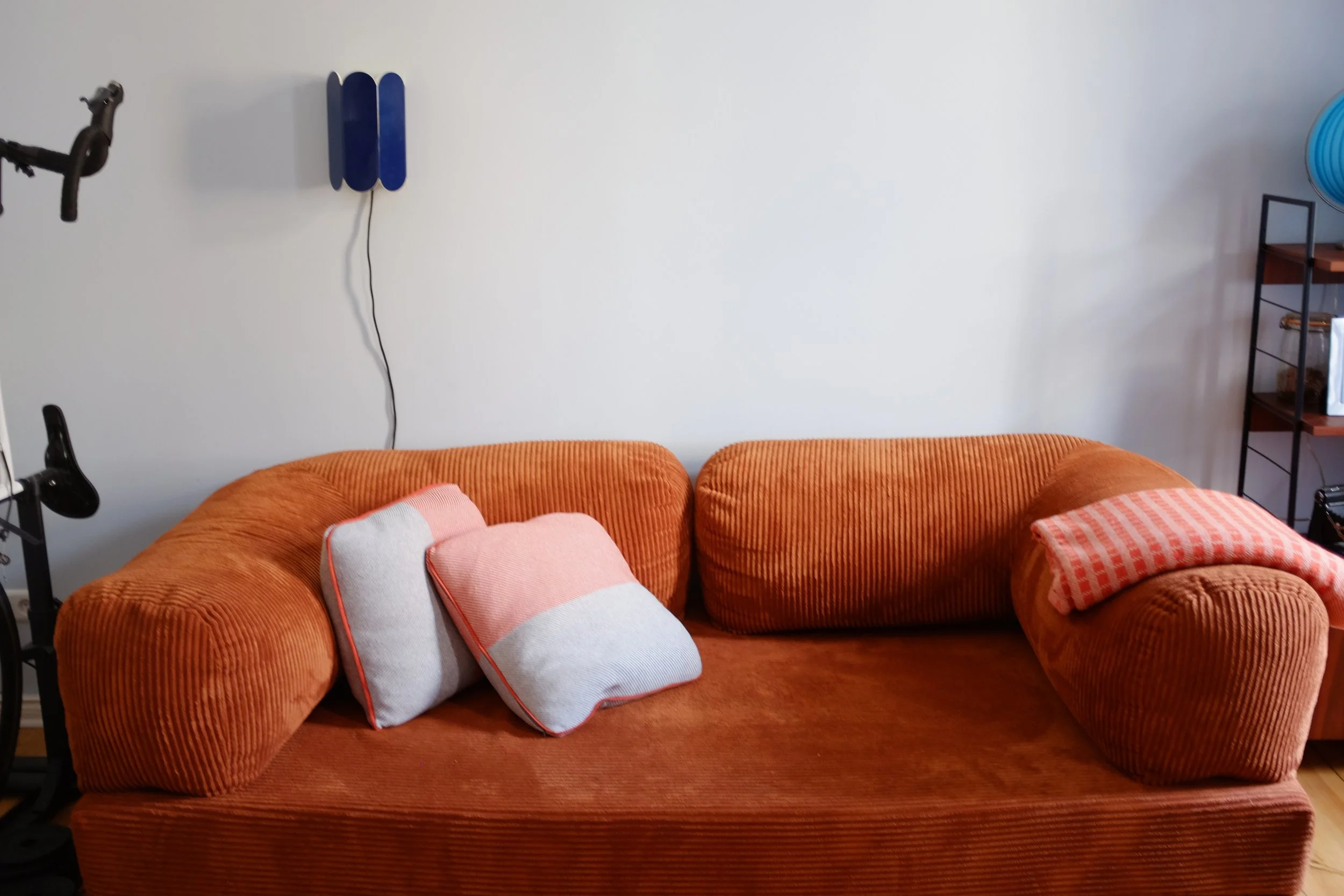 Orange corduroy sofa with blue Hay lamp in the background with a light blue wall