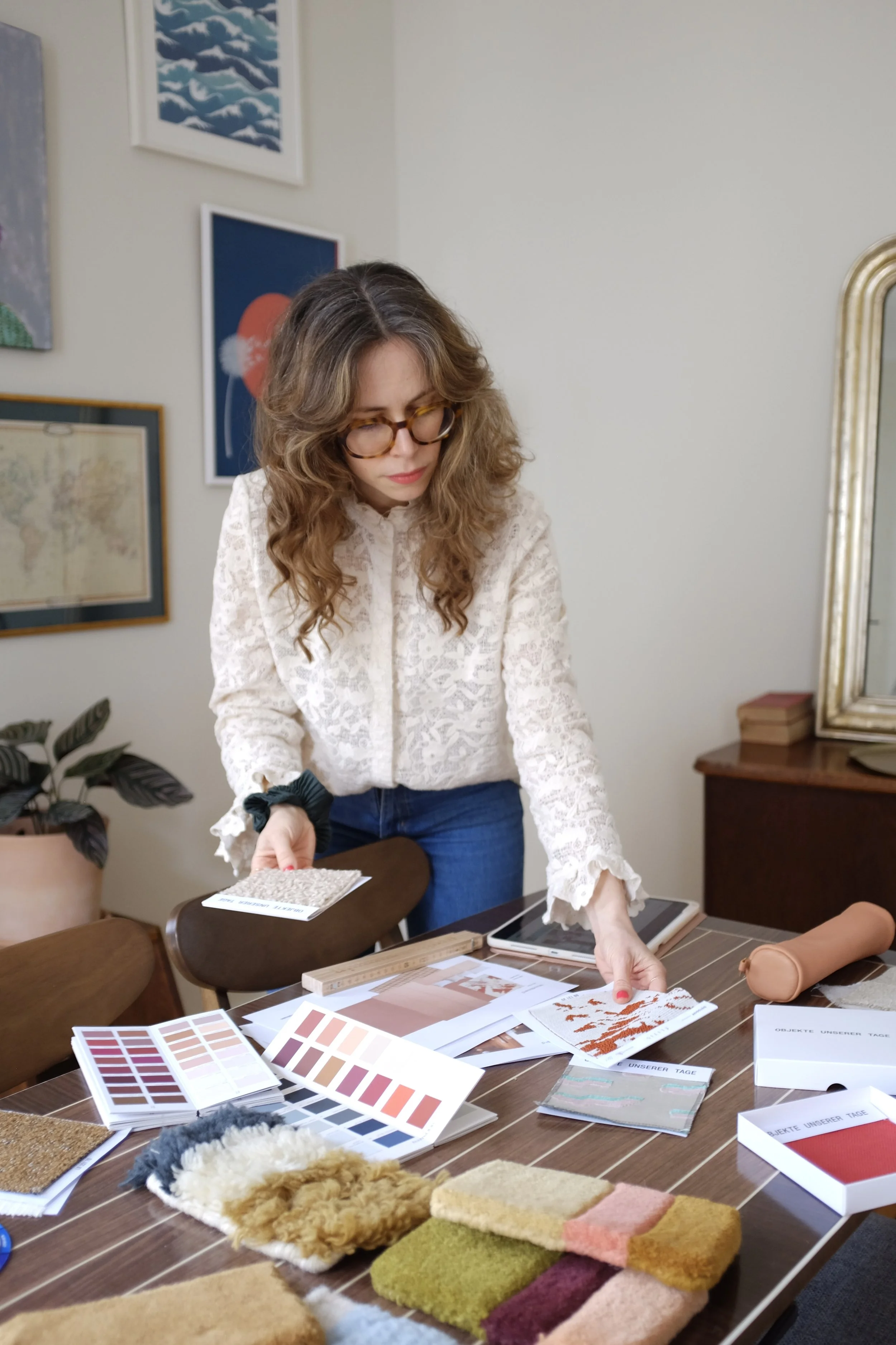 Frau mit Brille, die Farbmustern und Stoffproben auf einem Tisch in einem dekorativen Raum betrachtet.