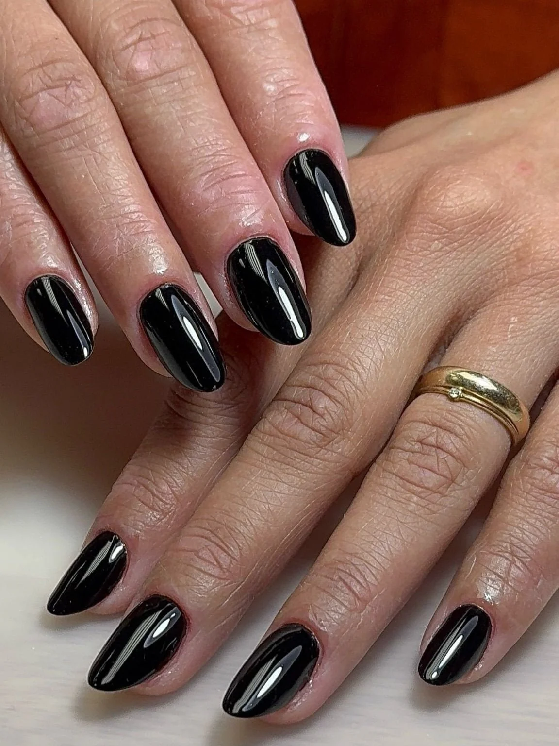Hands with almond-shaped, glossy black nails; one hand wears a gold ring—perfect inspiration for a chic tattoo studio look.