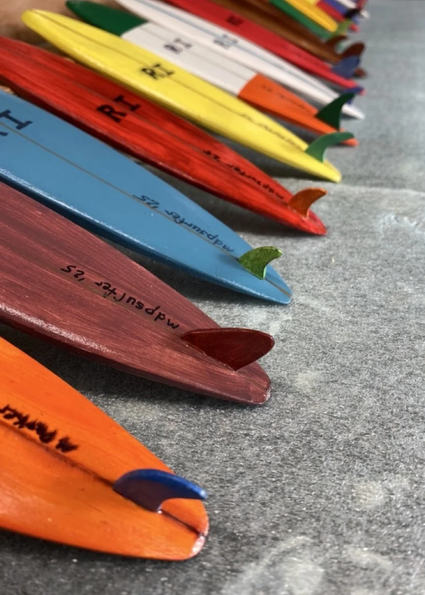 Colorful surfboards with fins on a sandy beach, arranged in a diagonal line.