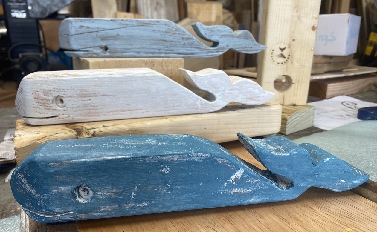 Wooden whale sculptures in various shades of blue and white on a workbench in a woodworking shop.