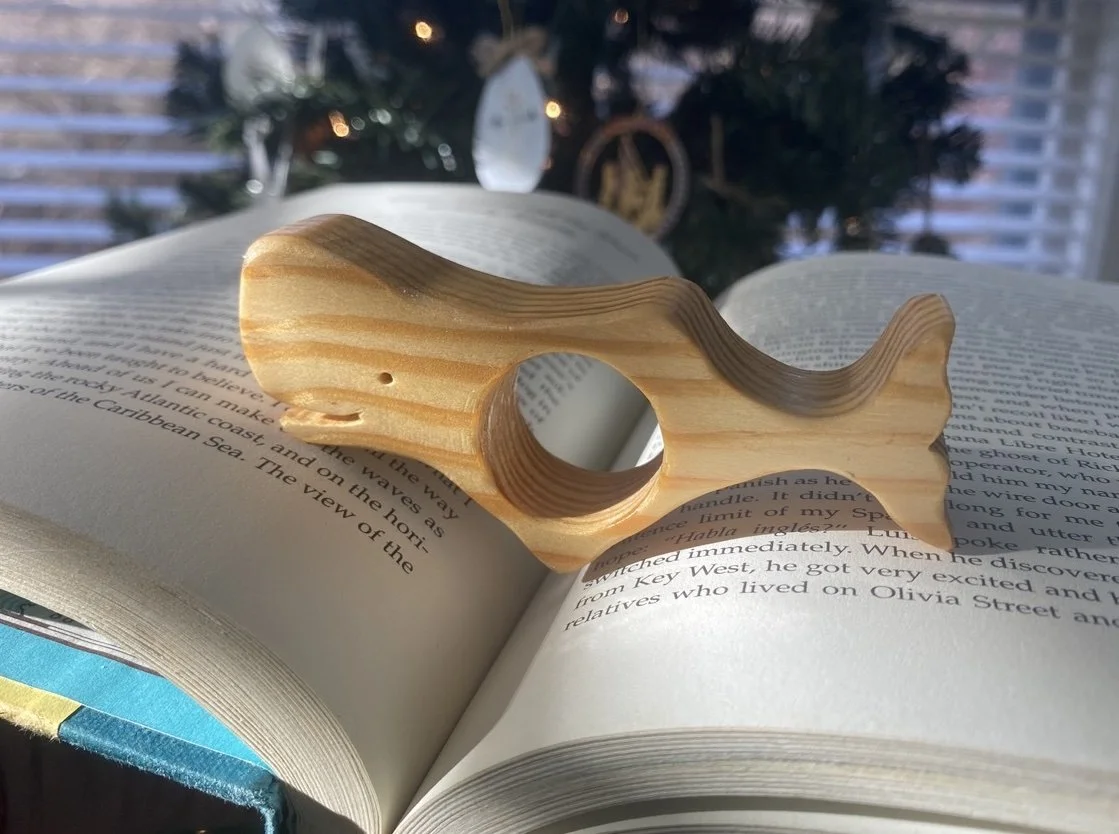 A wooden whale resting on an open book, with a decorated Christmas tree in the background.