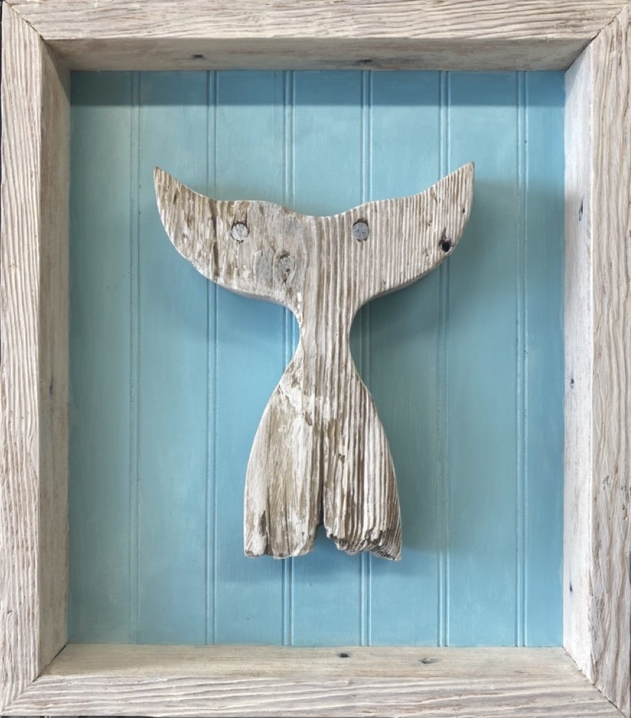 Wooden whale tail wall decor mounted inside a square wooden frame with a light blue background.
