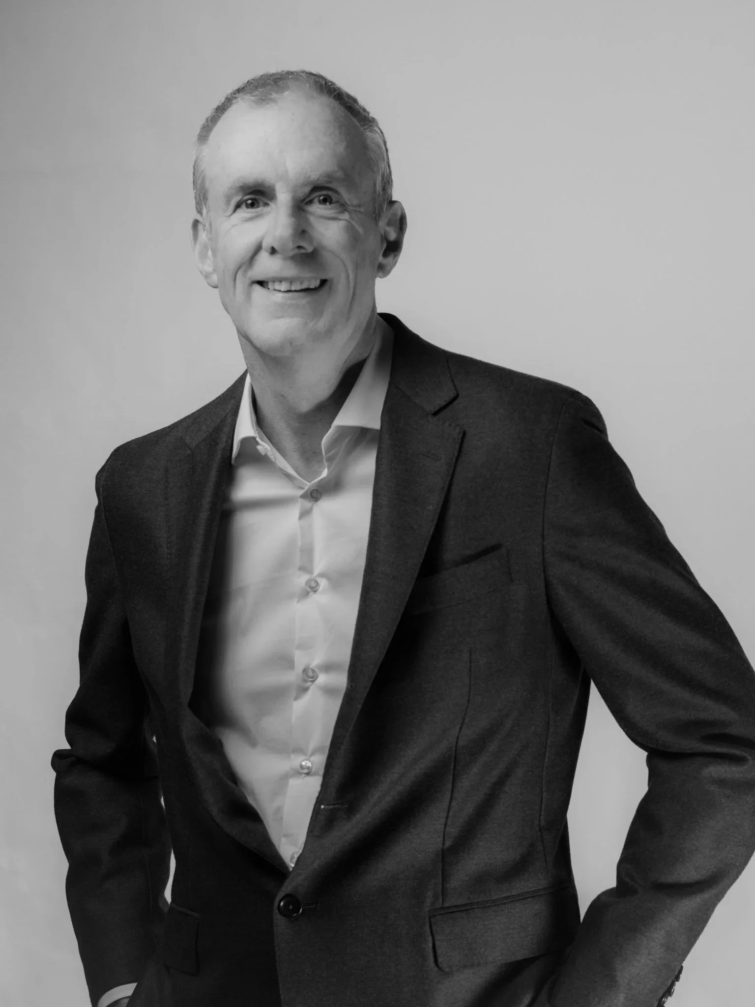 Black and white photo of a smiling person, wearing a dark sweater, a white undershirt, and a necklace with a pendant.