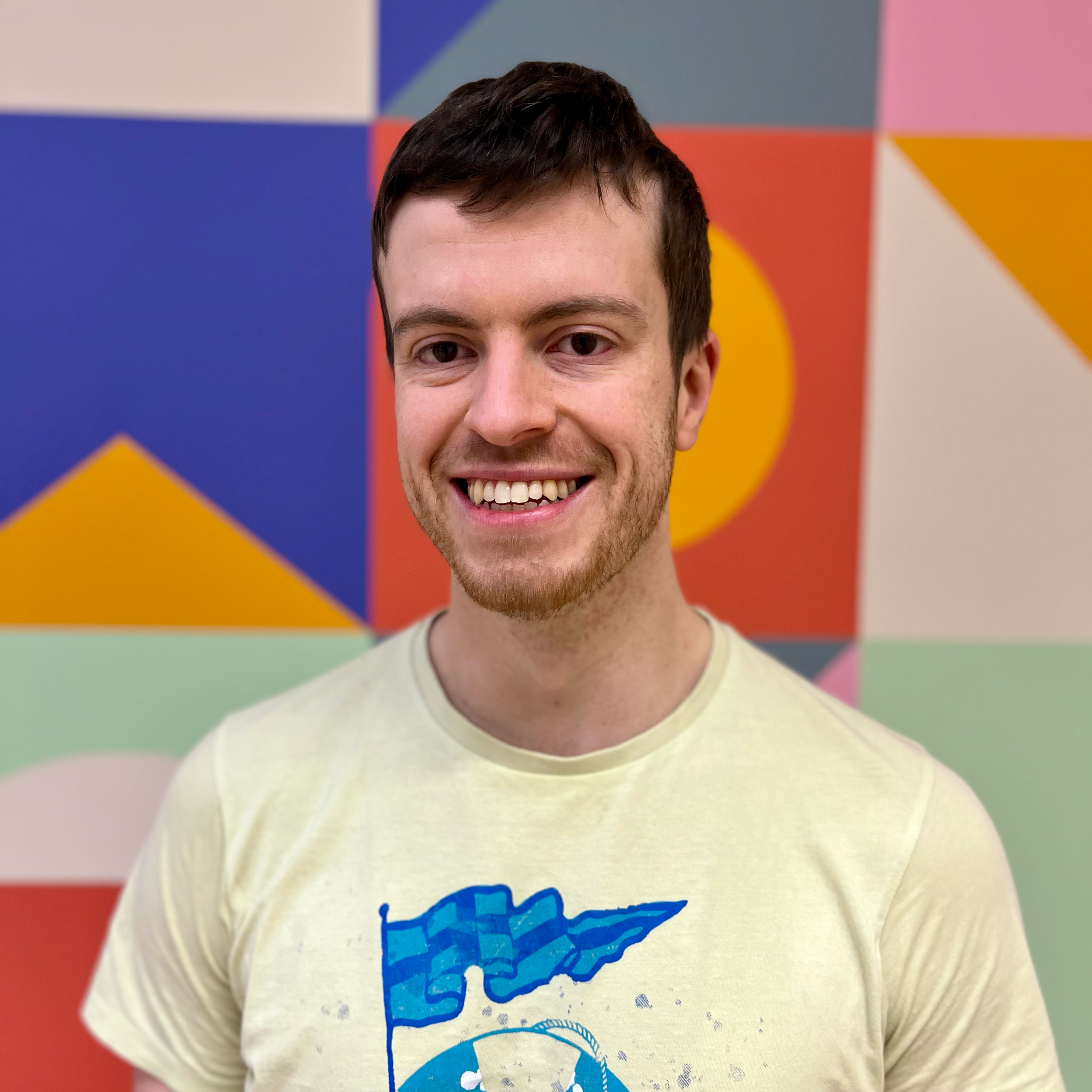 Smiling man in a light-colored shirt with a geometric-patterned background.
