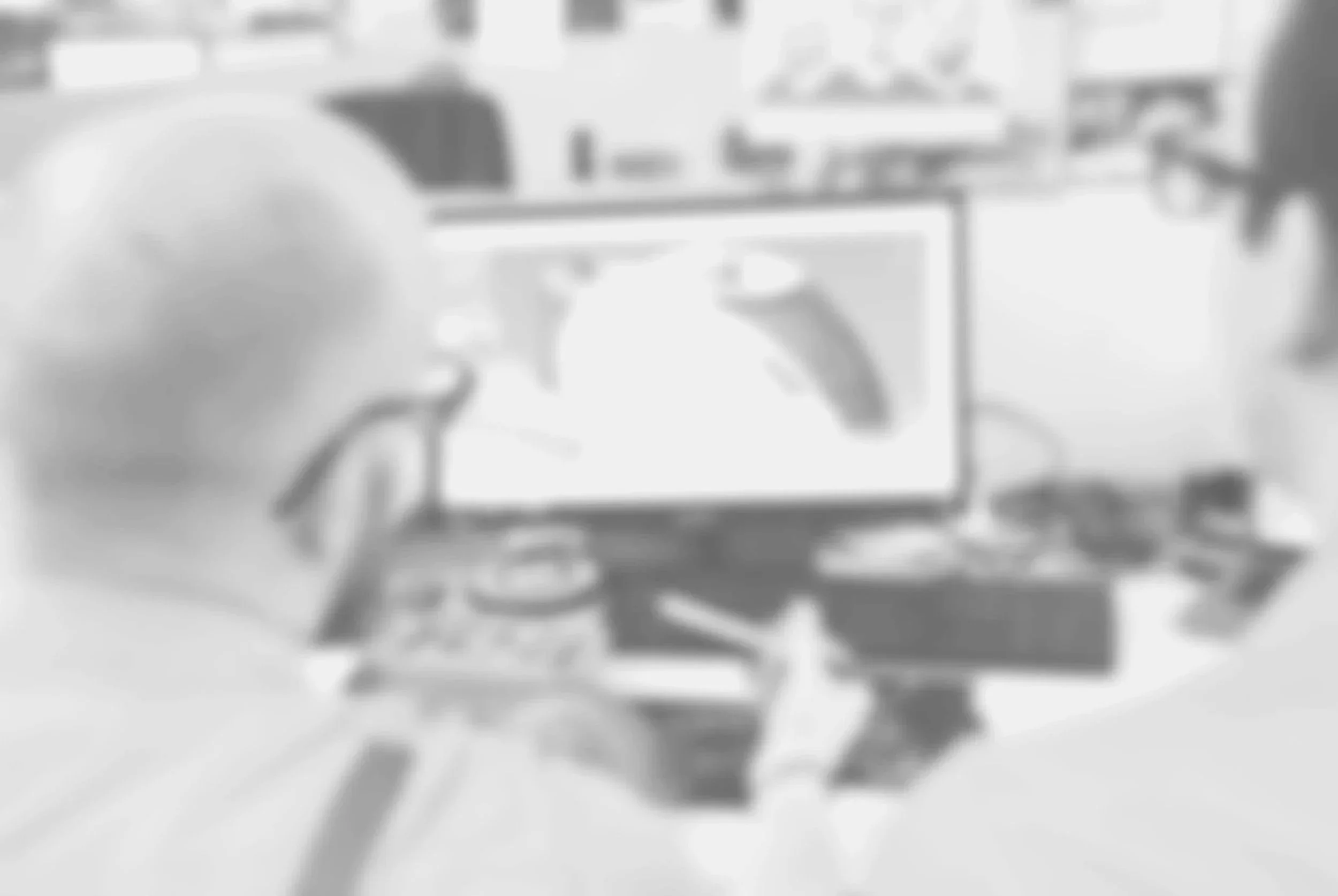 Two people seated at a desk with electronics, one on the left using a laptop, the other on the right using a desktop monitor.