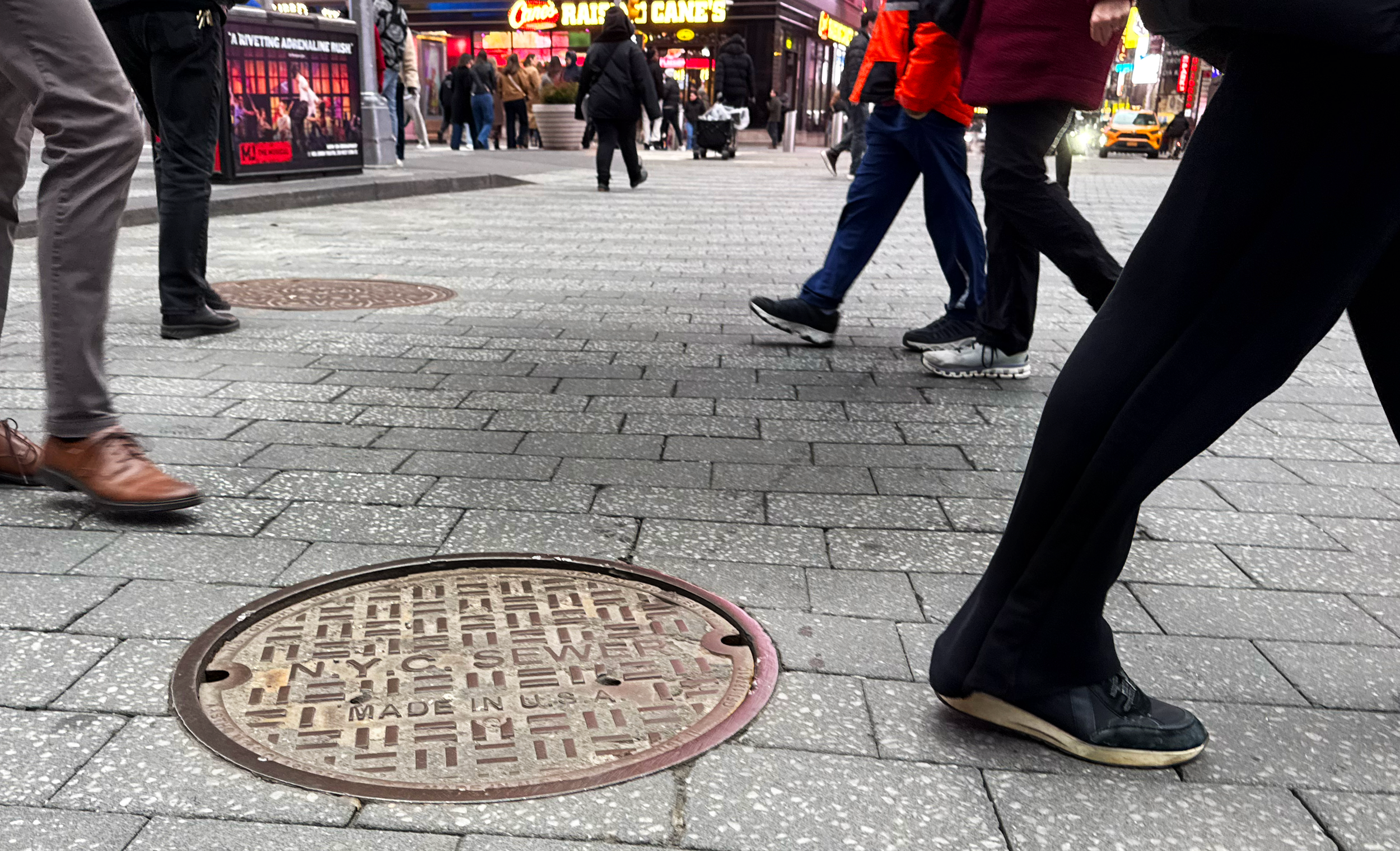 People walking past a NYC sewer manhole cover. 