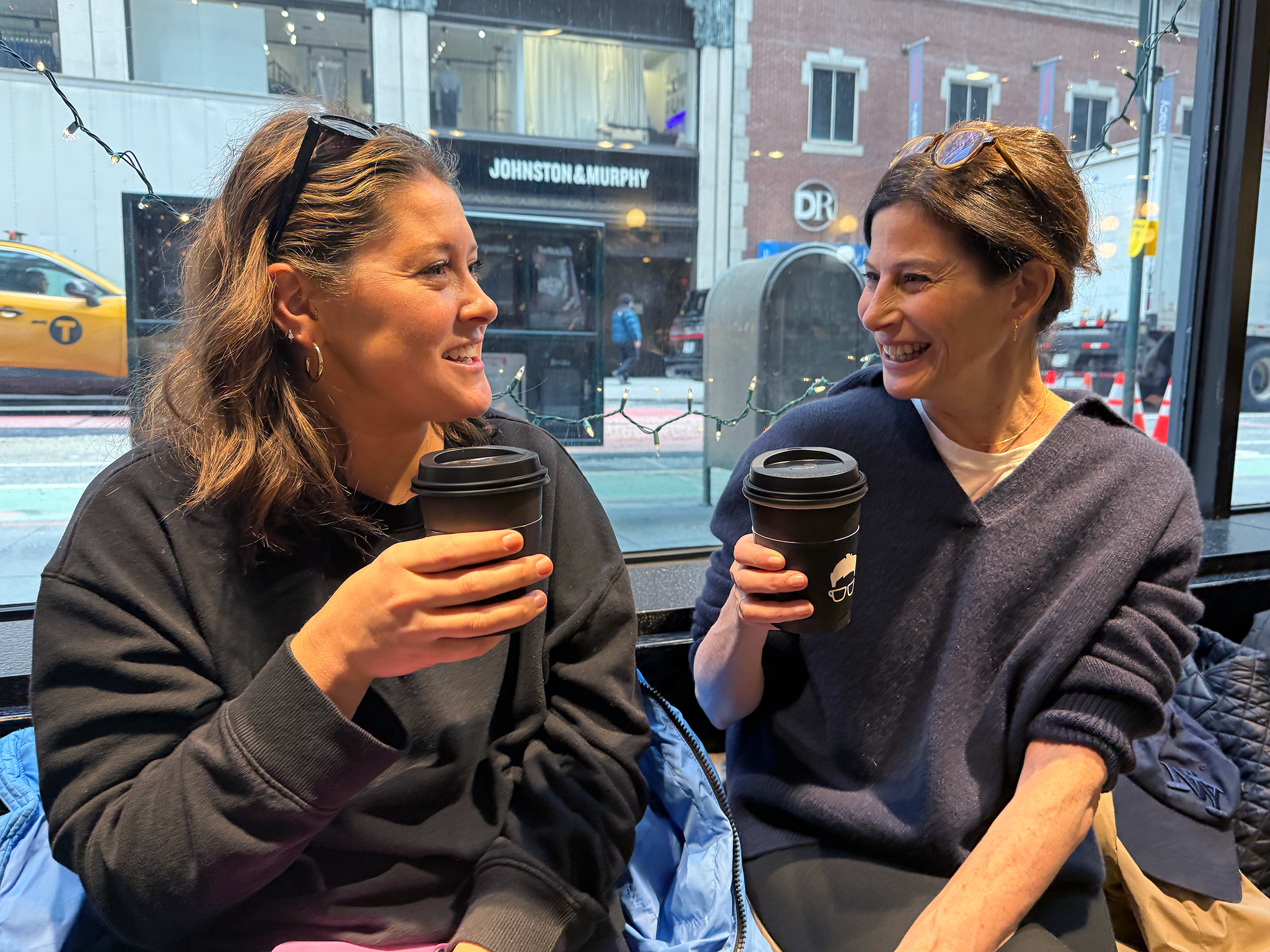 Two women laughing as they drink coffee in a local coffee shop
