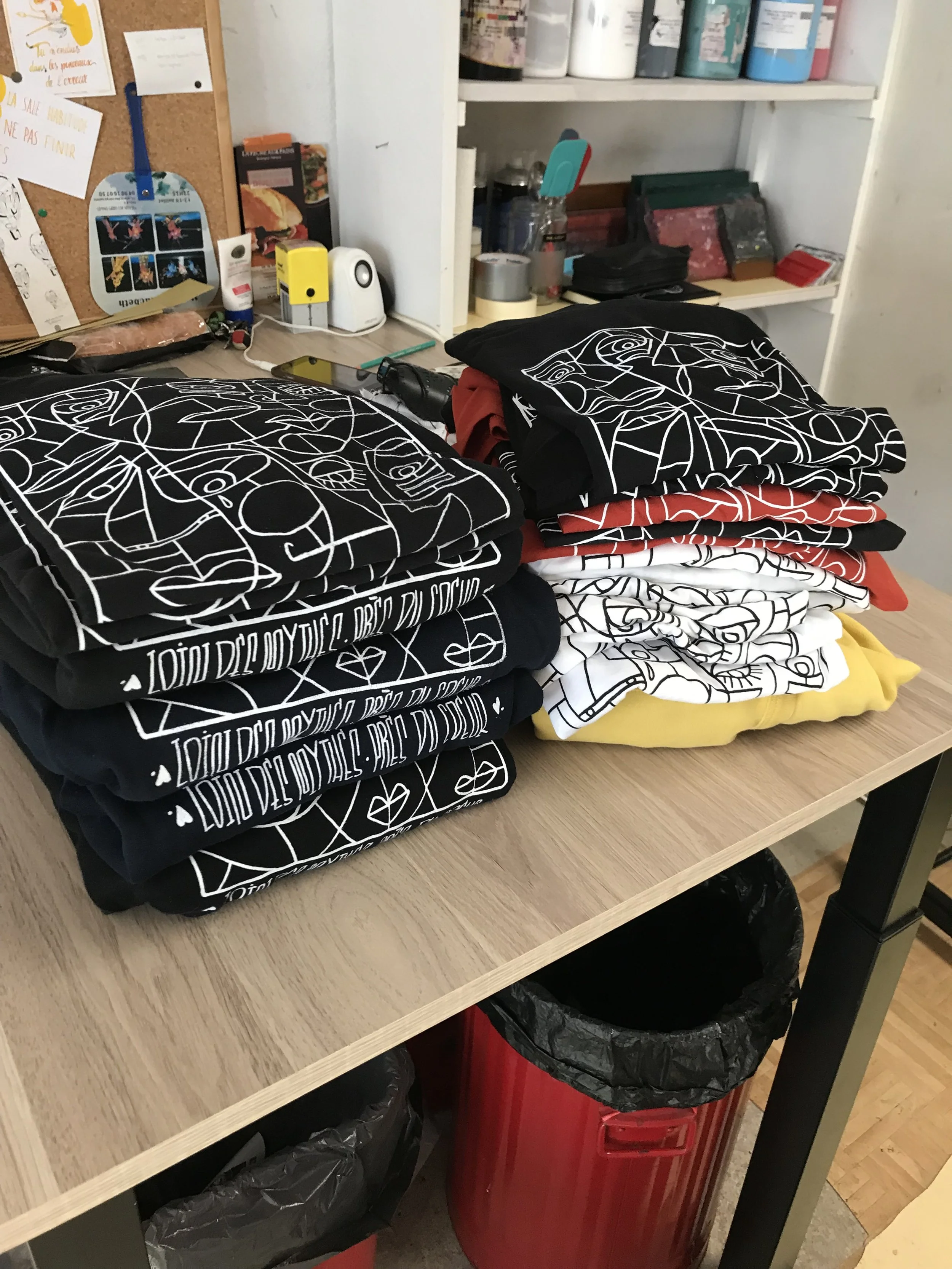 Pile de vêtements pliés avec des motifs graphiques en noir, blanc, rouge, jaune et gris sur un bureau en bois.