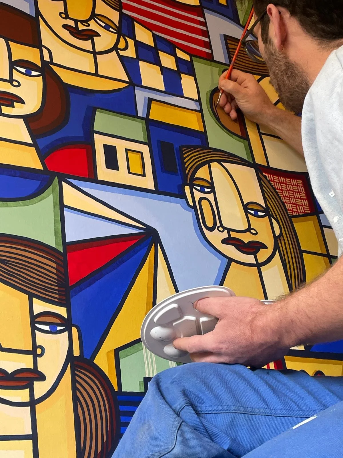 Un artiste peignant une peinture abstraite avec des formes géométriques et des visages stylisés en couleurs vives.