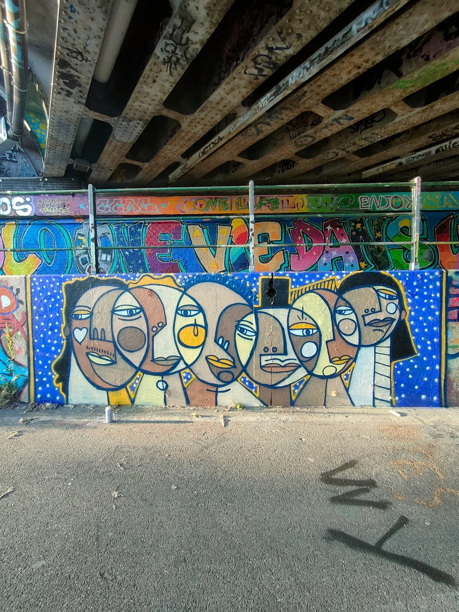 Graffiti artistique représentant un groupe de femmes stylisées avec des visages expressifs, couleurs vives et fond bleu with dots.