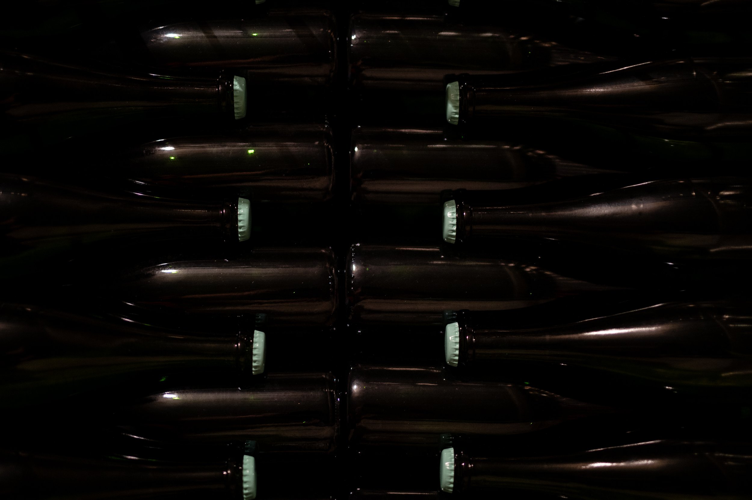 Une rangée de bouteilles de bière en verre noir, alignées horizontalement dans un espace sombre.