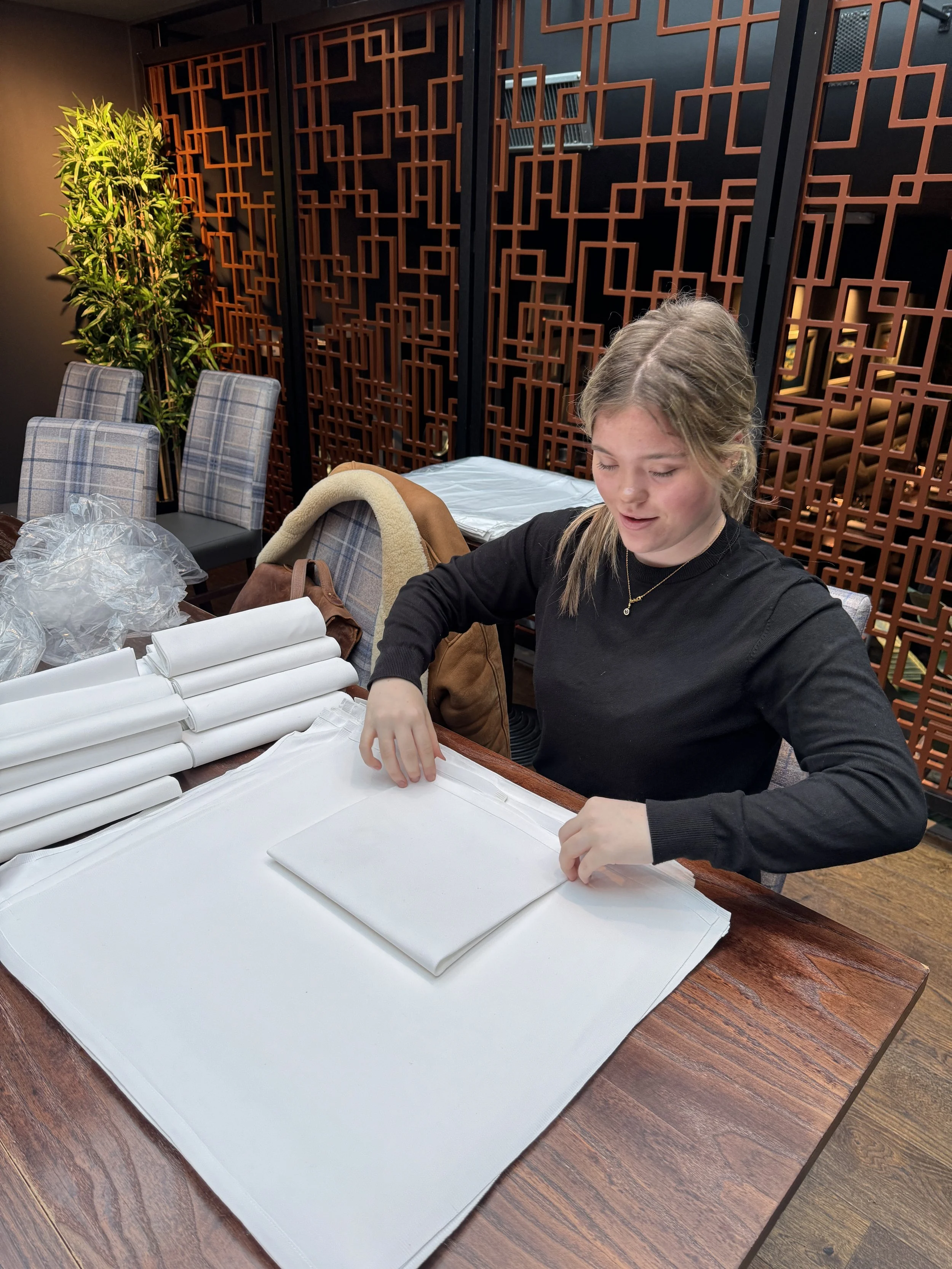 A waitress in a white shirt and black pants carrying two plates of food in a restaurant with wooden furniture and tables.