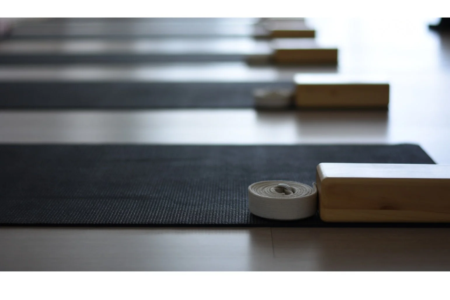 Yoga mats with wooden blocks and rolled-up straps on a black mat in a yoga studio.