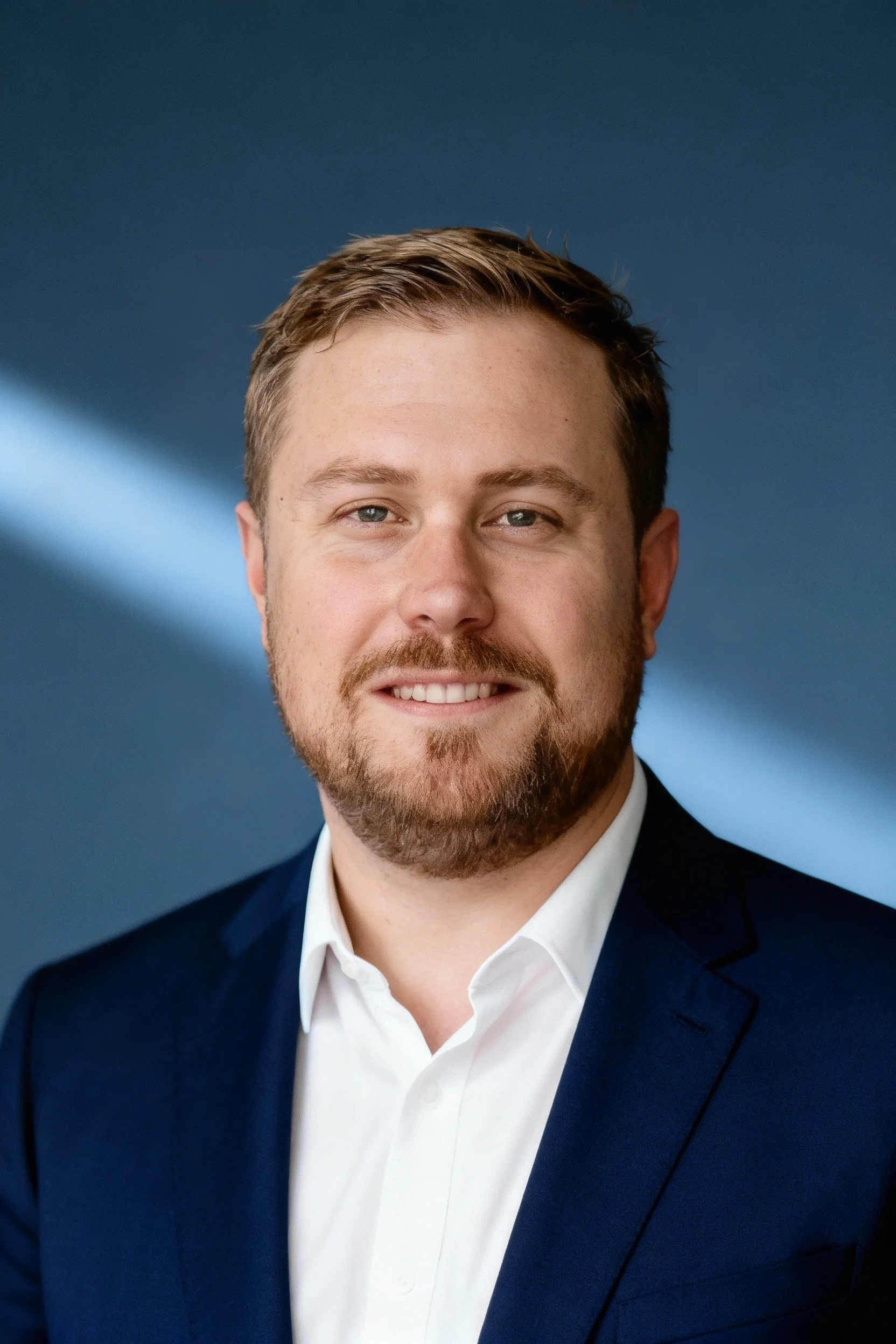 Man in a gray suit with a light green tie standing outdoors next to a grassy-textured wall.