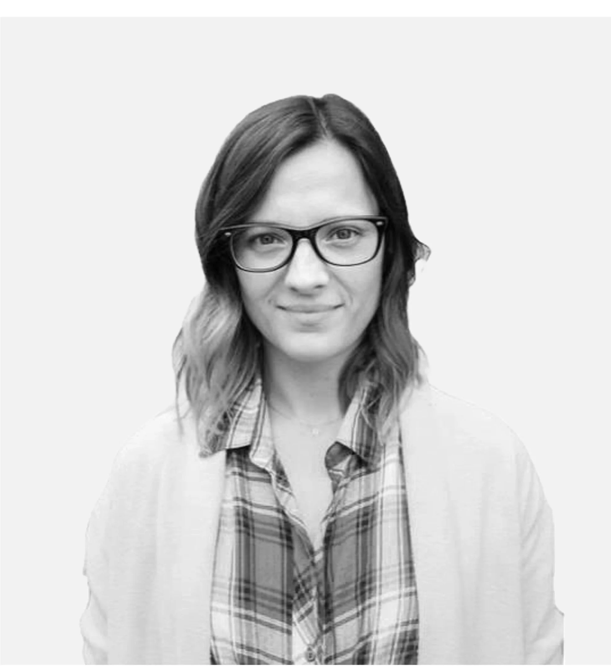 Black and white photo of a person with glasses, long hair, wearing a plaid shirt and cardigan.