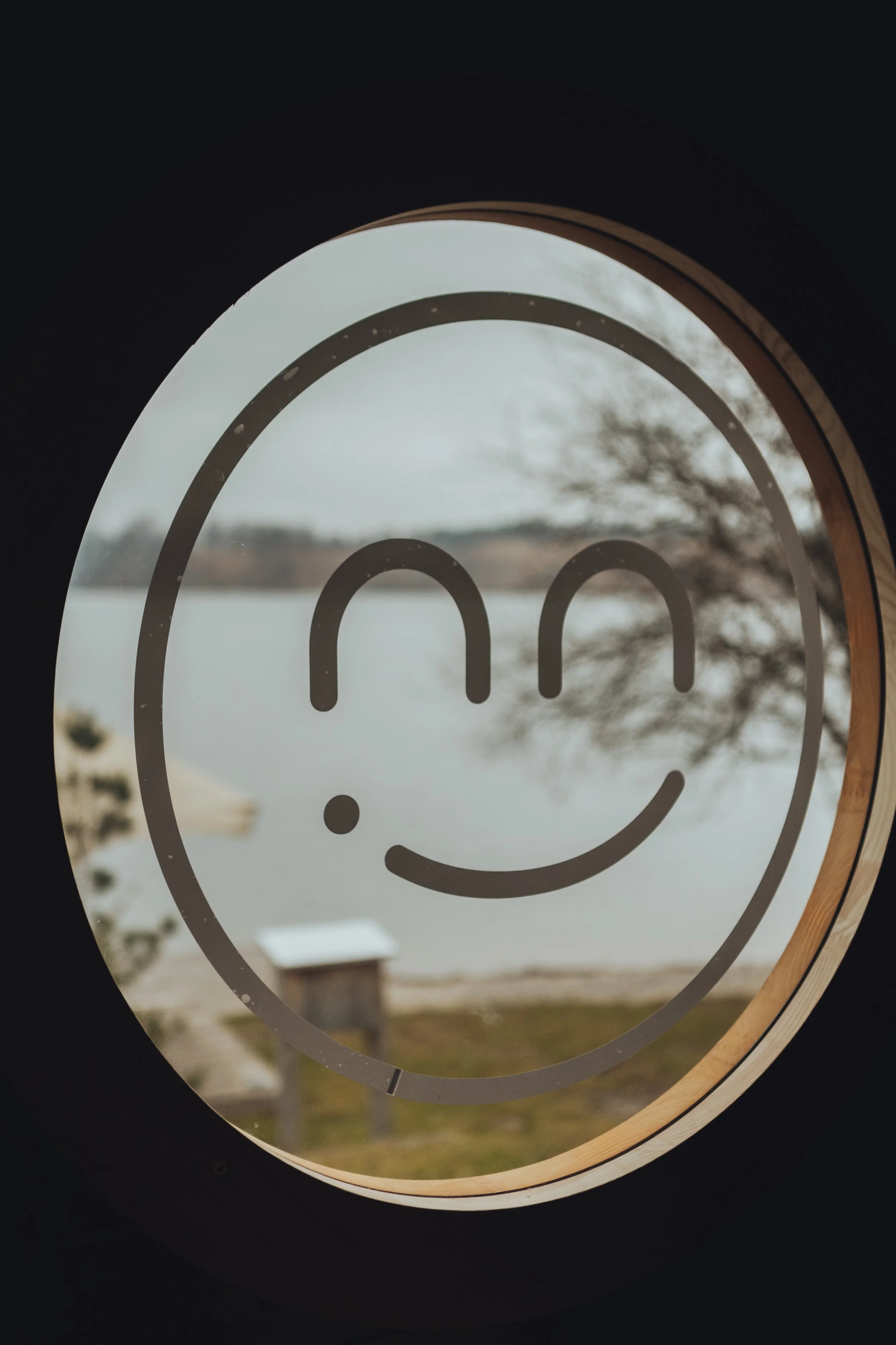 A circular window with a smiley face logo, showing a lake and trees outside.