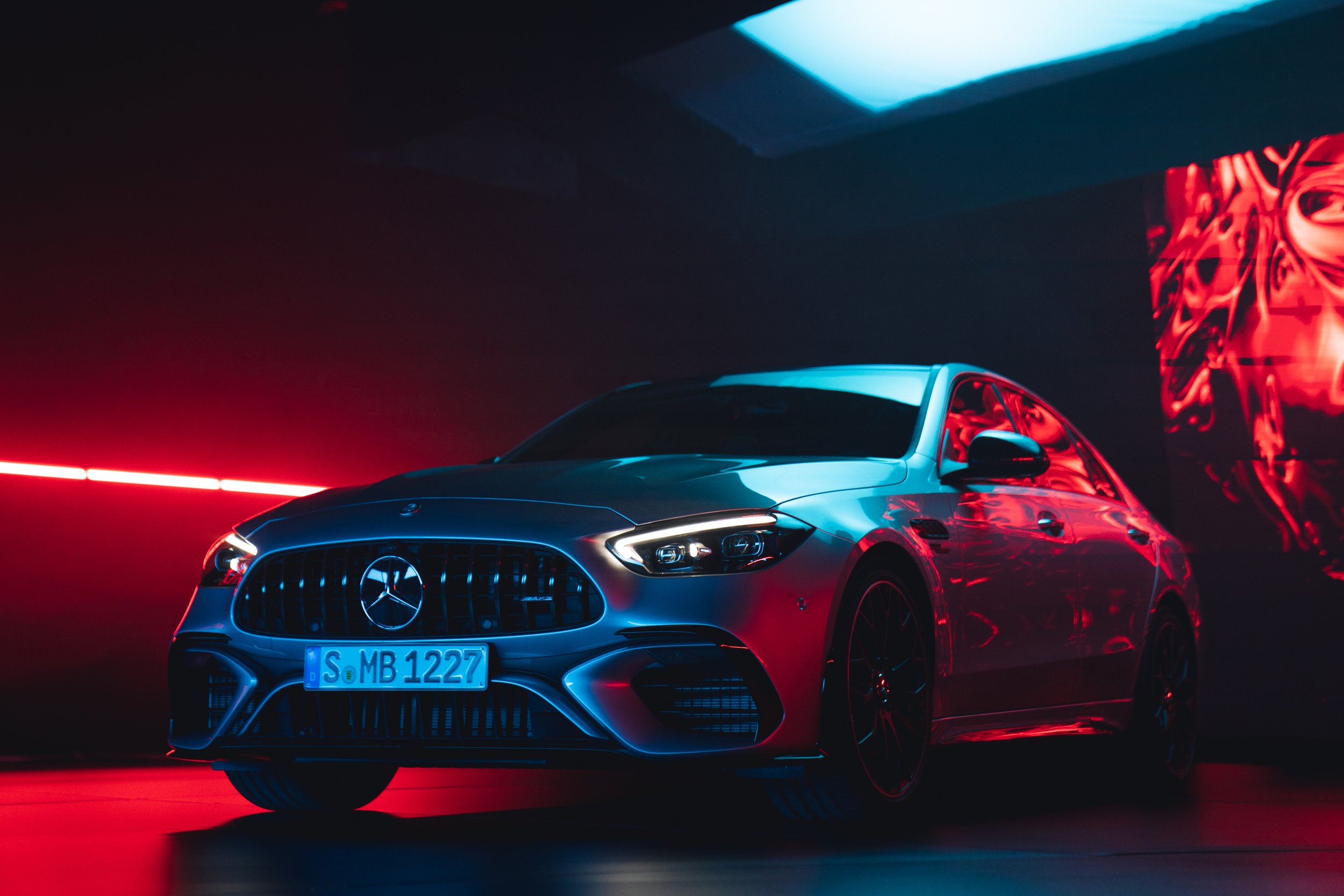 A silver Mercedes-Benz car inside a dark room with red and blue lighting, showcasing it's front and side profile.