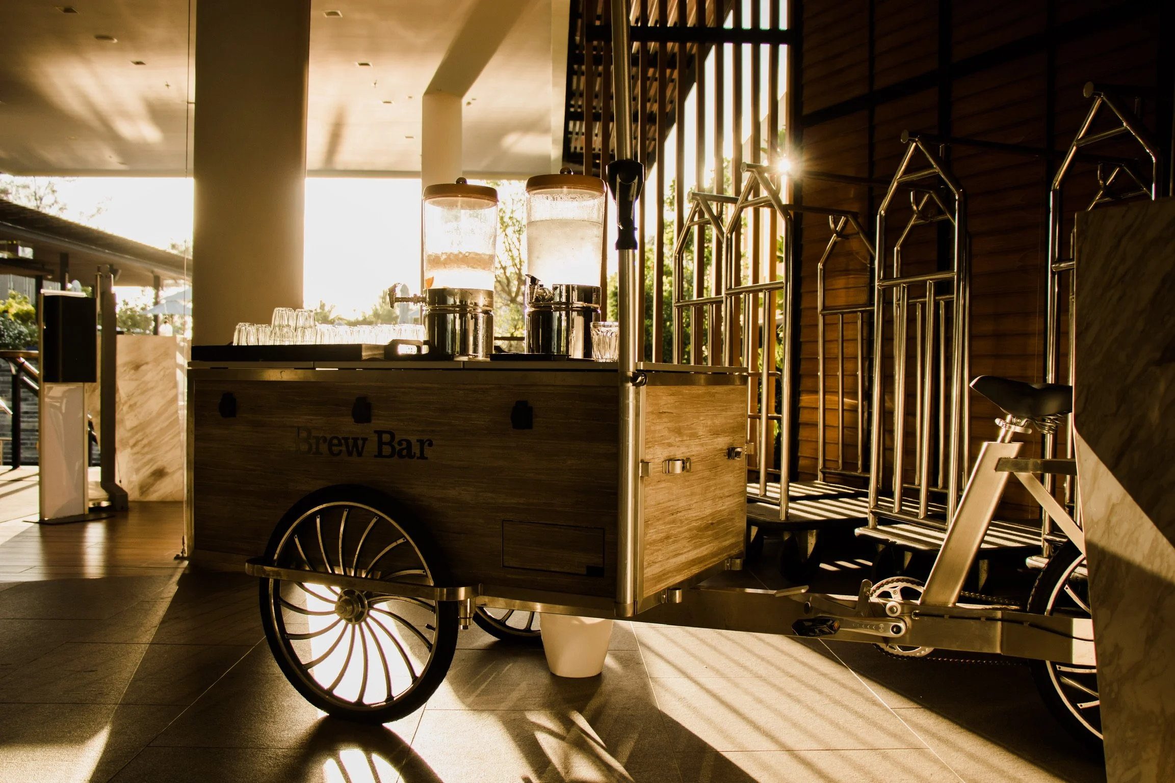 Brew bar on a cargo bicycle, with glass containers, in a sunlit indoor space with wooden walls.