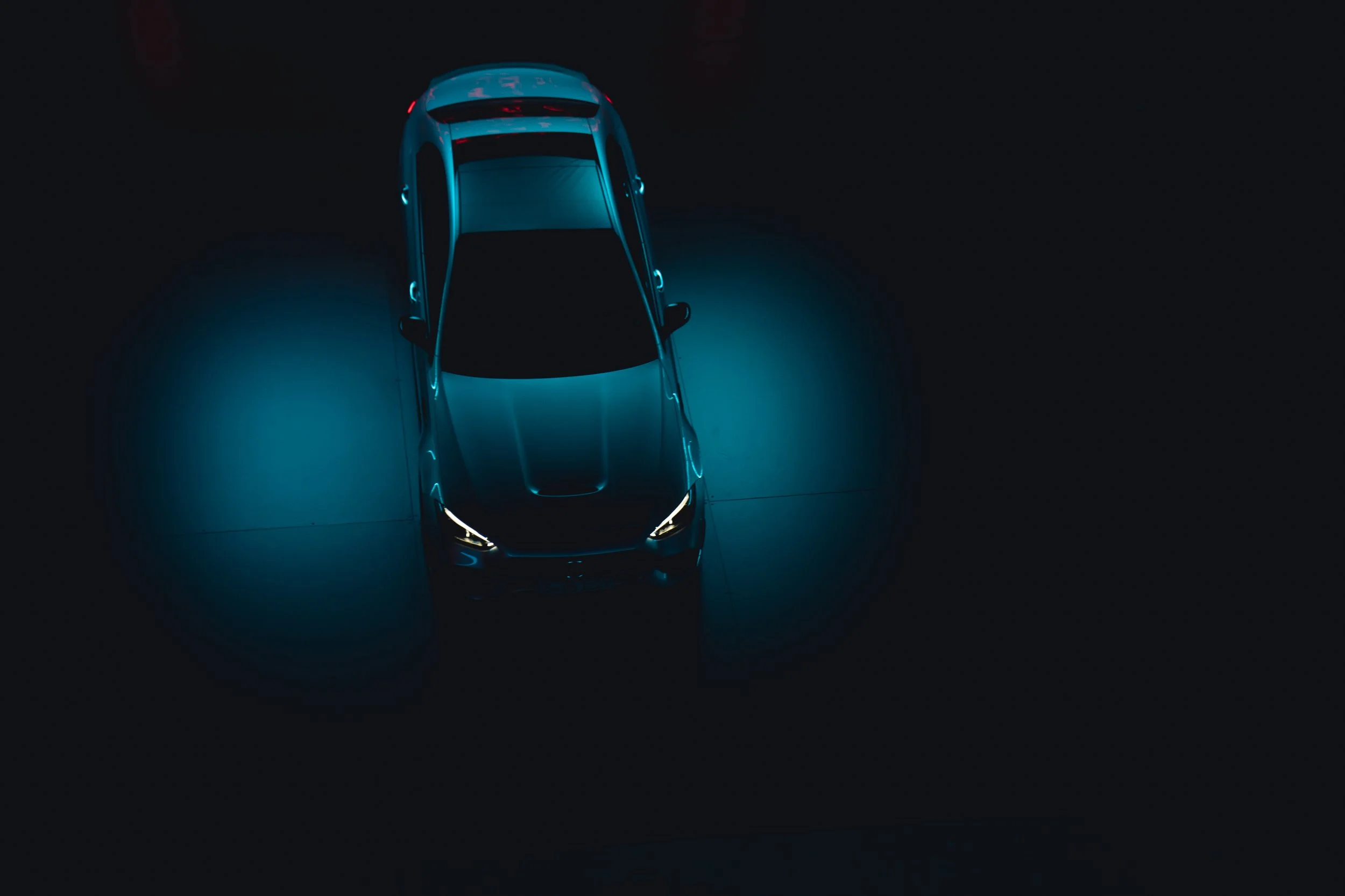 An overhead view of a car illuminated with blue lighting in a dark setting.