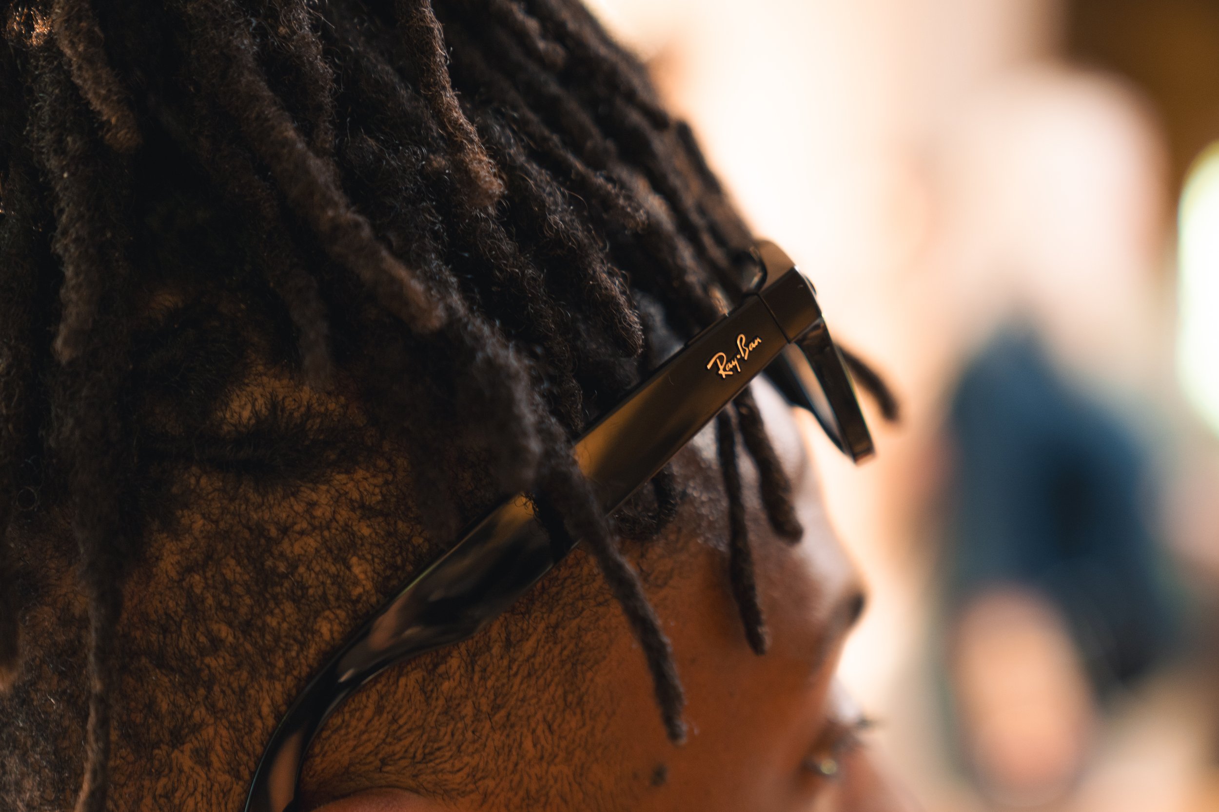 Close-up of a person with dreadlocks wearing black Ray-Ban glasses.
