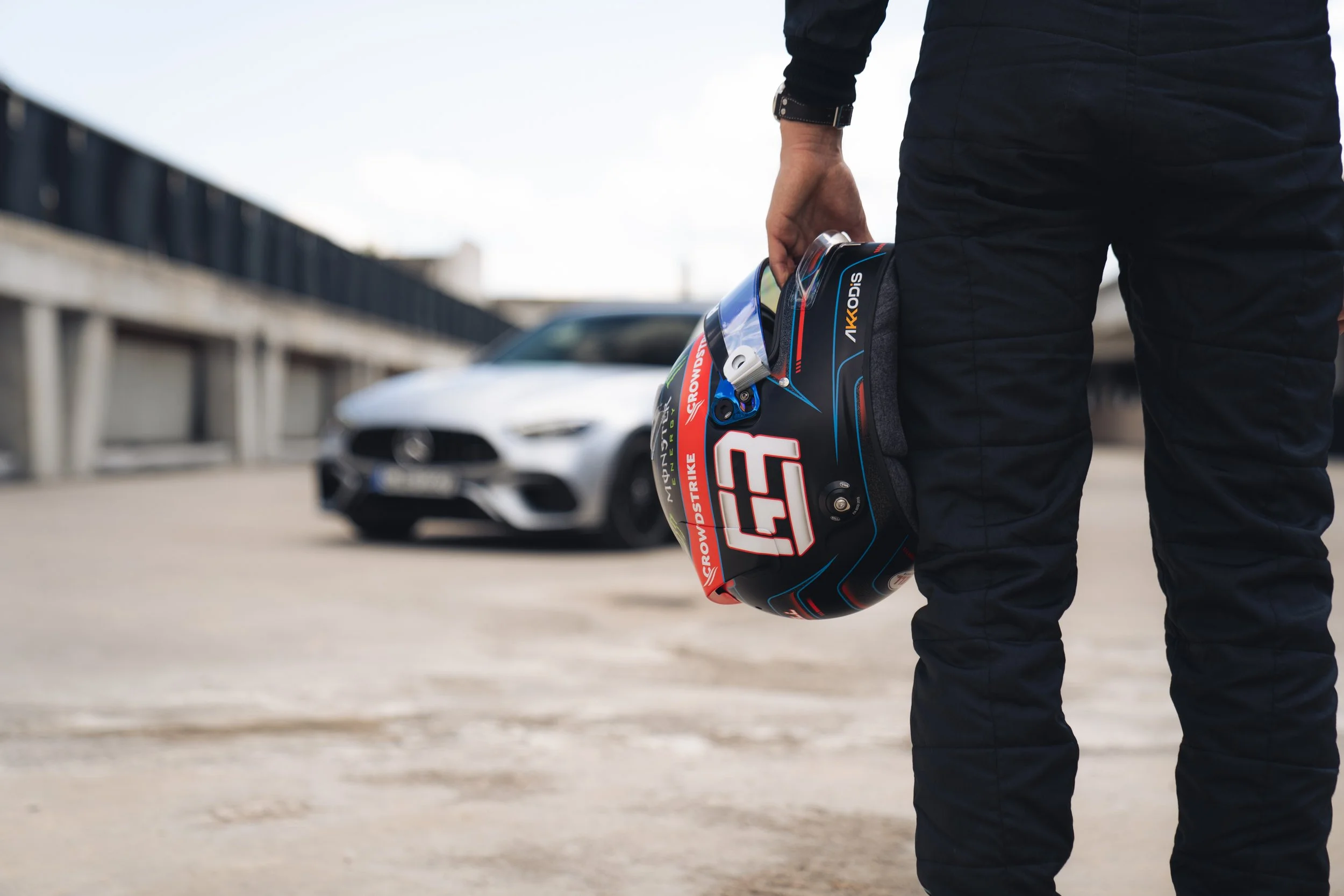Person holding a racing helmet in front of a white luxury car on a parking lot.