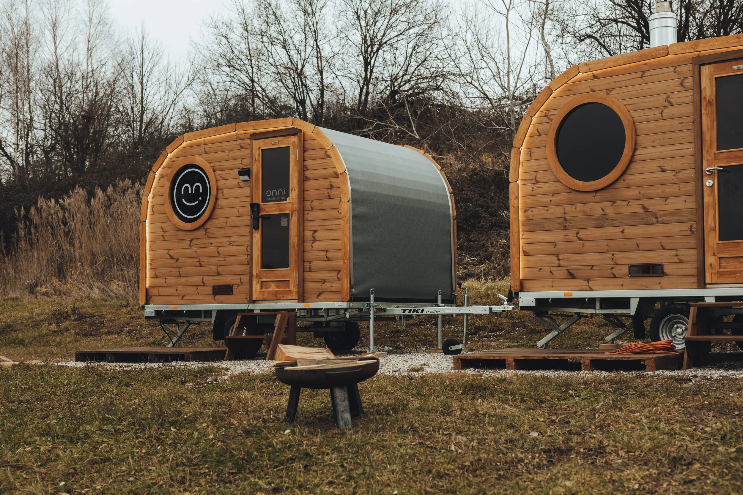 Two wooden tiny houses on trailers outdoors with trees in the background.