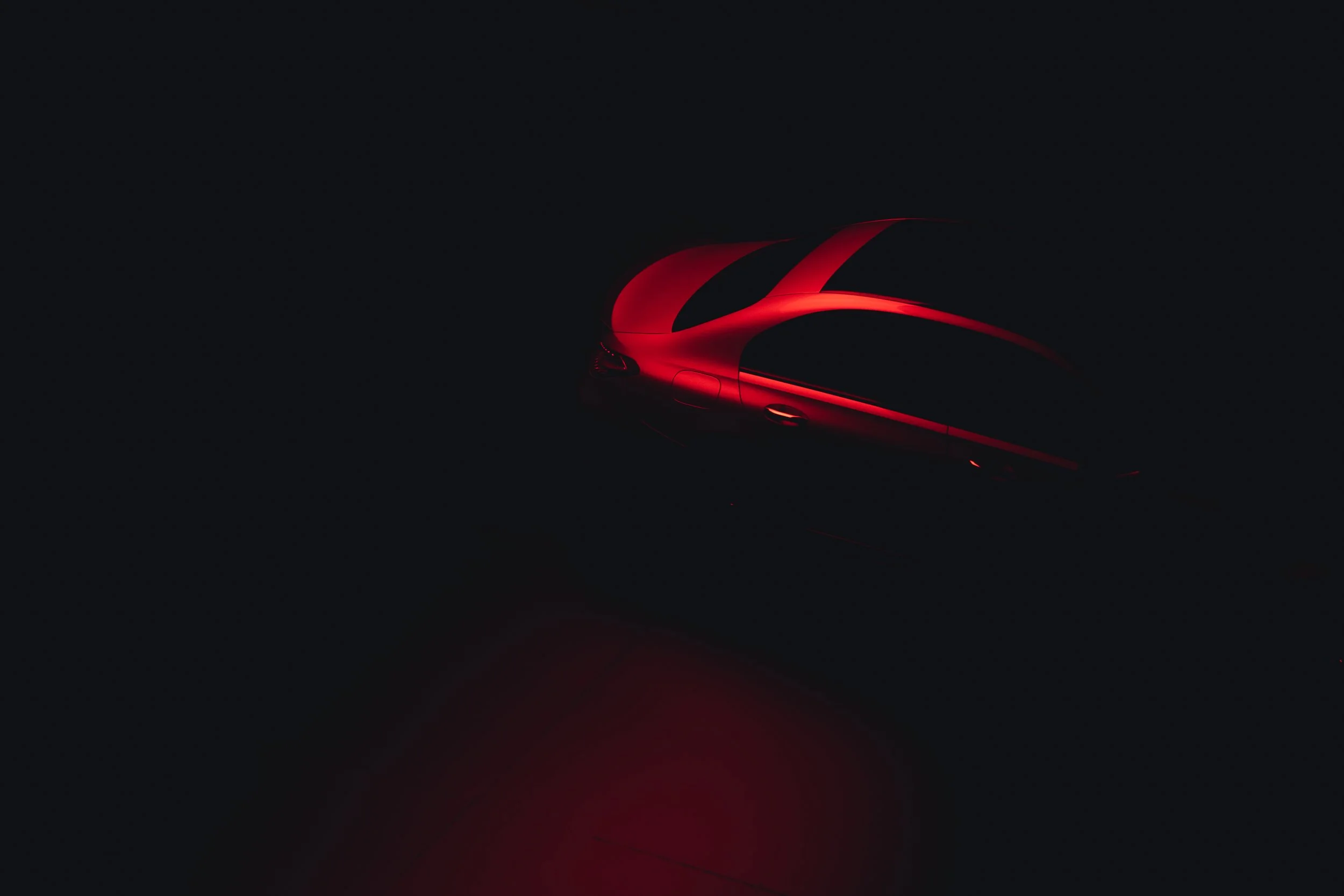 A dark image of a sleek red sports car, partially illuminated, emphasizing its curves and design.