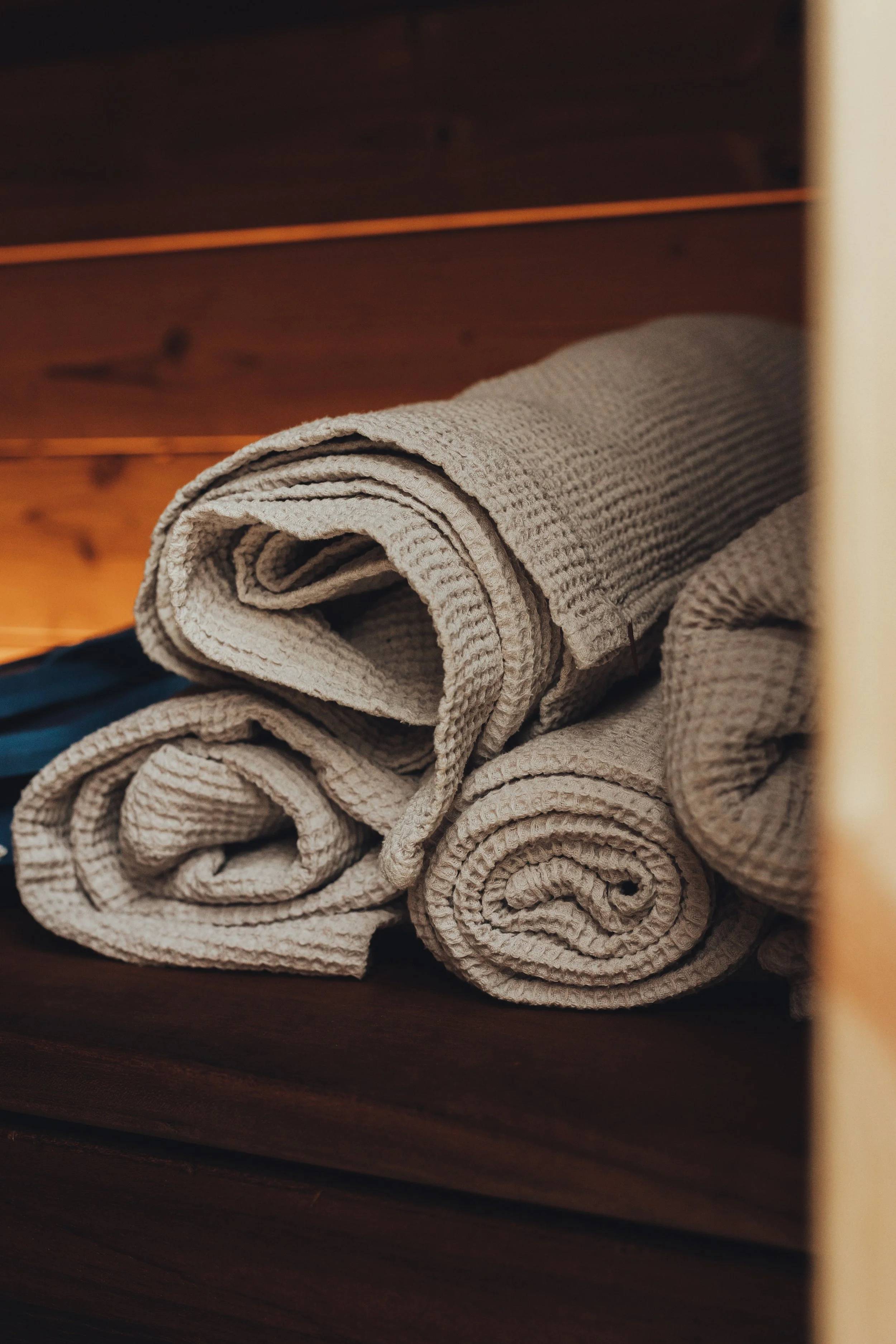 Four beige rolled-up waffle-textured towels on a wooden shelf