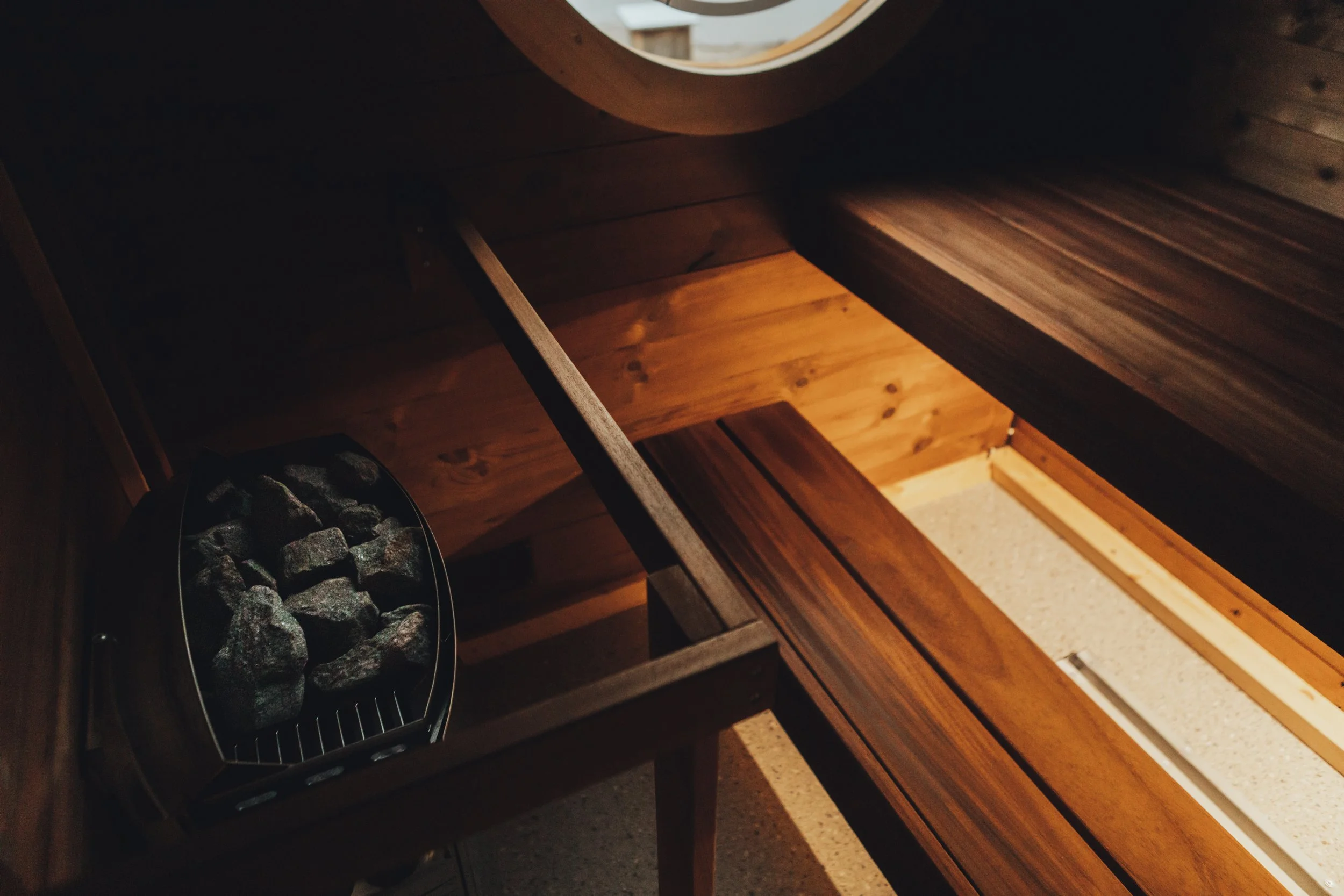Interior of a sauna with wooden benches and a heater filled with stones.