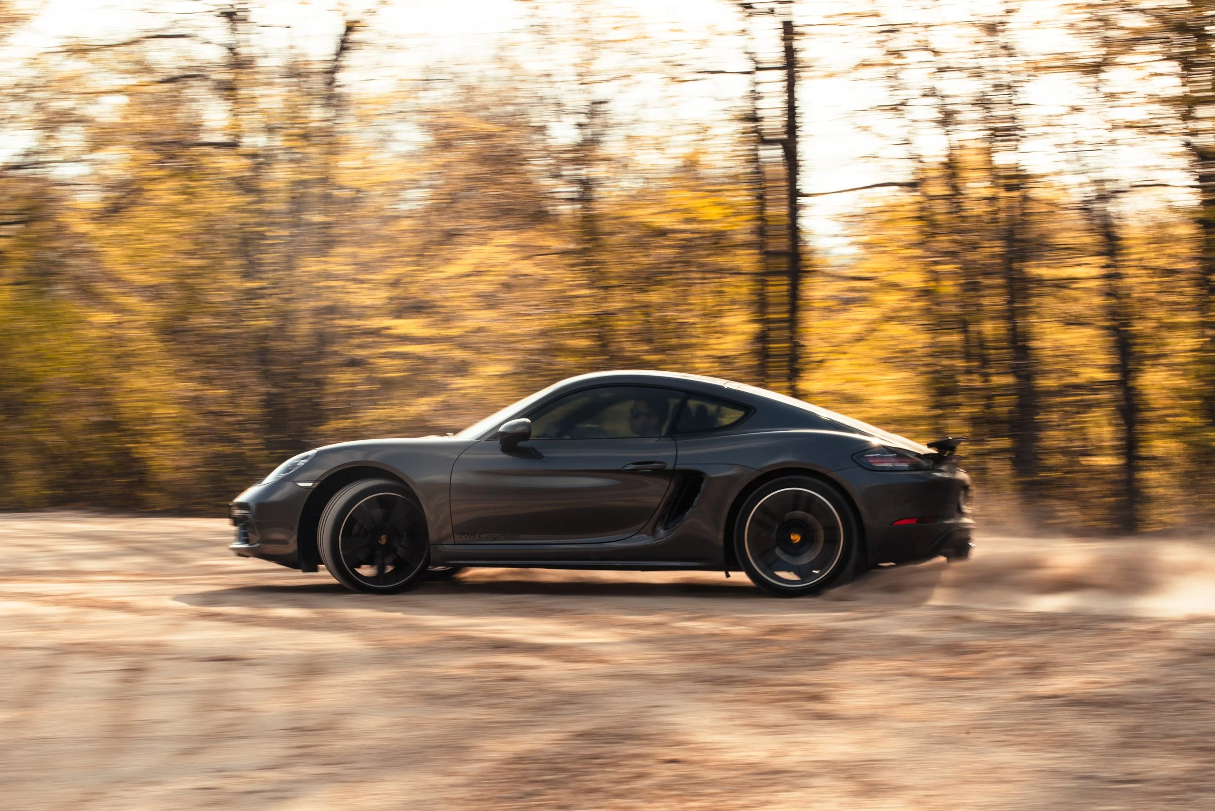 A black sports car driving on a dirt road during fall with trees in the background and blurred motion