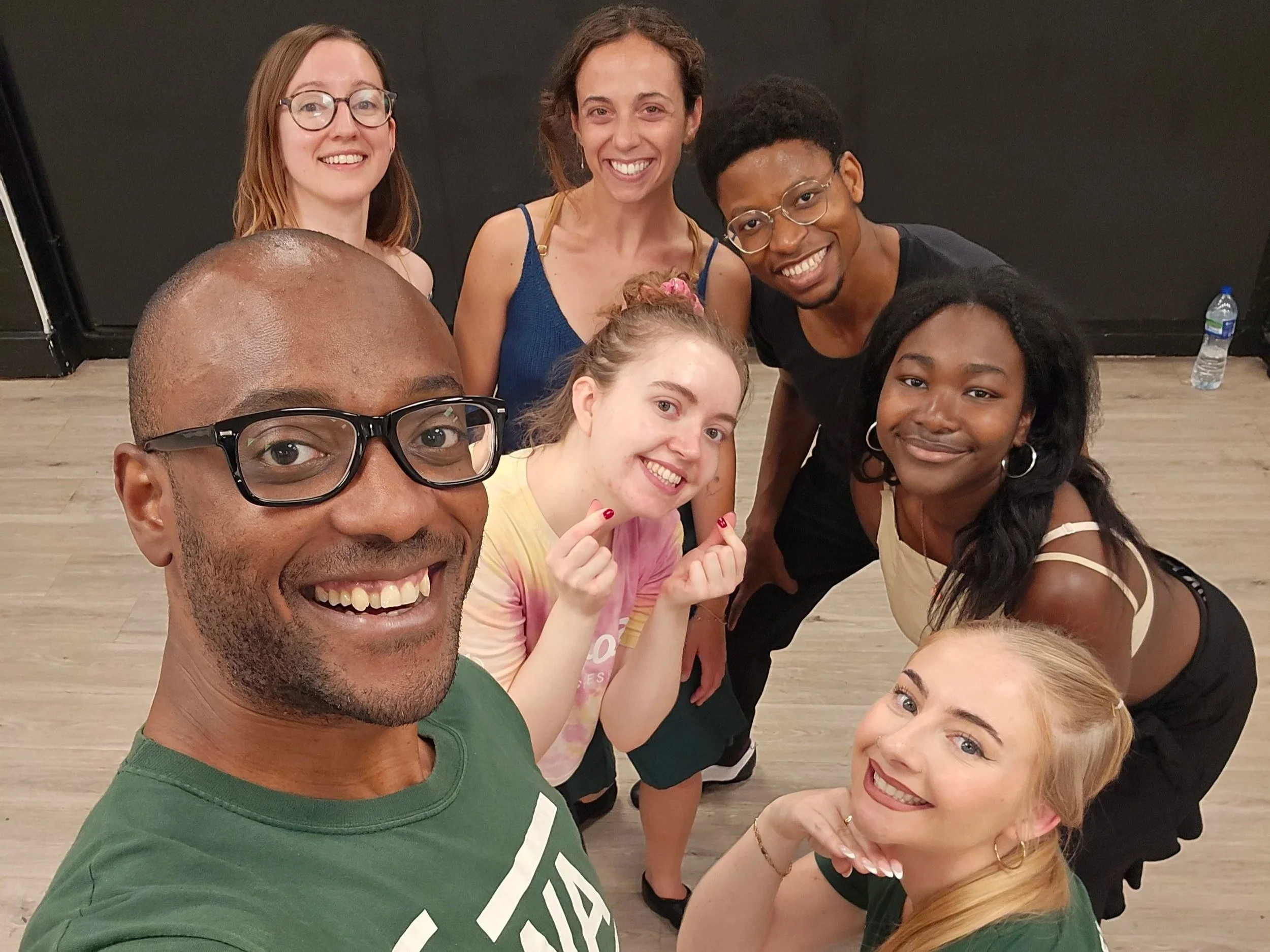 Smiling diverse group of people taking a selfie in a salsa dance studio or event space.