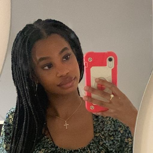 Young woman taking a selfie in a mirror using a red phone case, wearing a floral top and a cross necklace.