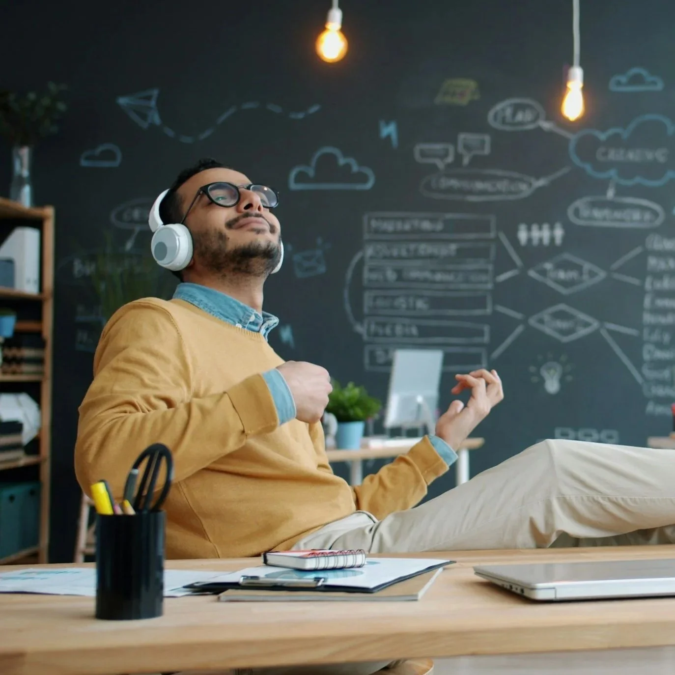 man wearing headphones and playing the air guitar while sitting at his desk