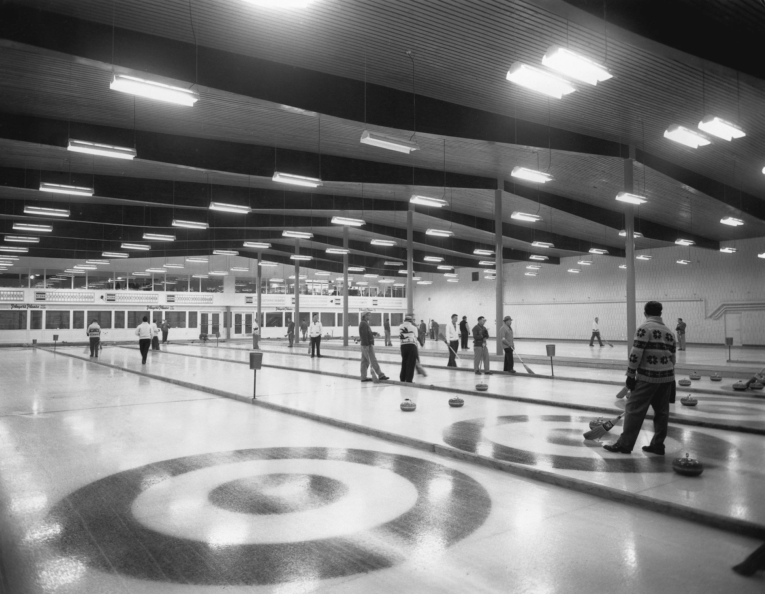 An indoor curling rink with people curling and sweeping stones on the ice.