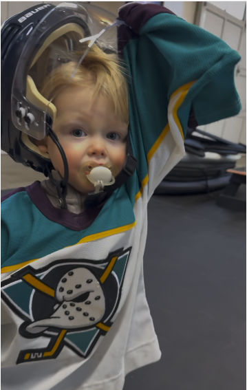 Young boy in a hockey jersey wearing a medical helmet with a chin strap at a hospital or clinic.