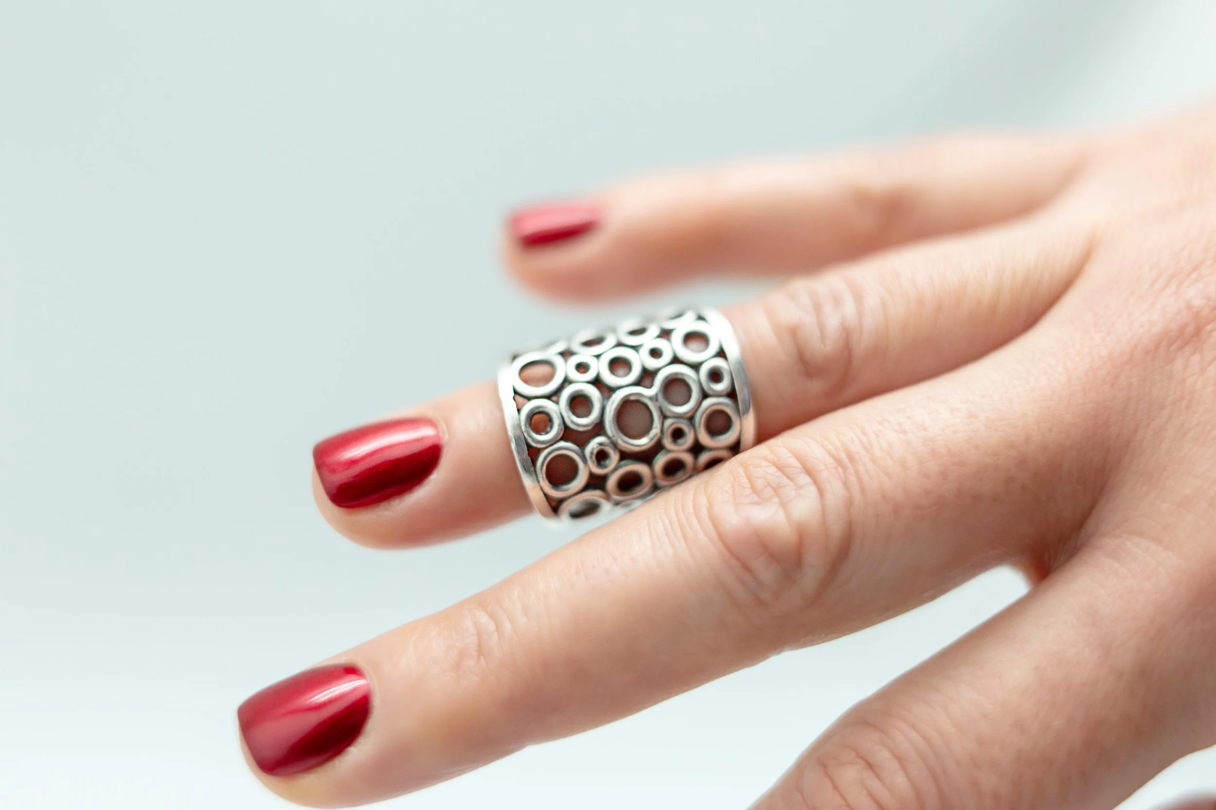Close-up of a hand with red nail polish wearing a silver ring with circular patterns on a finger.