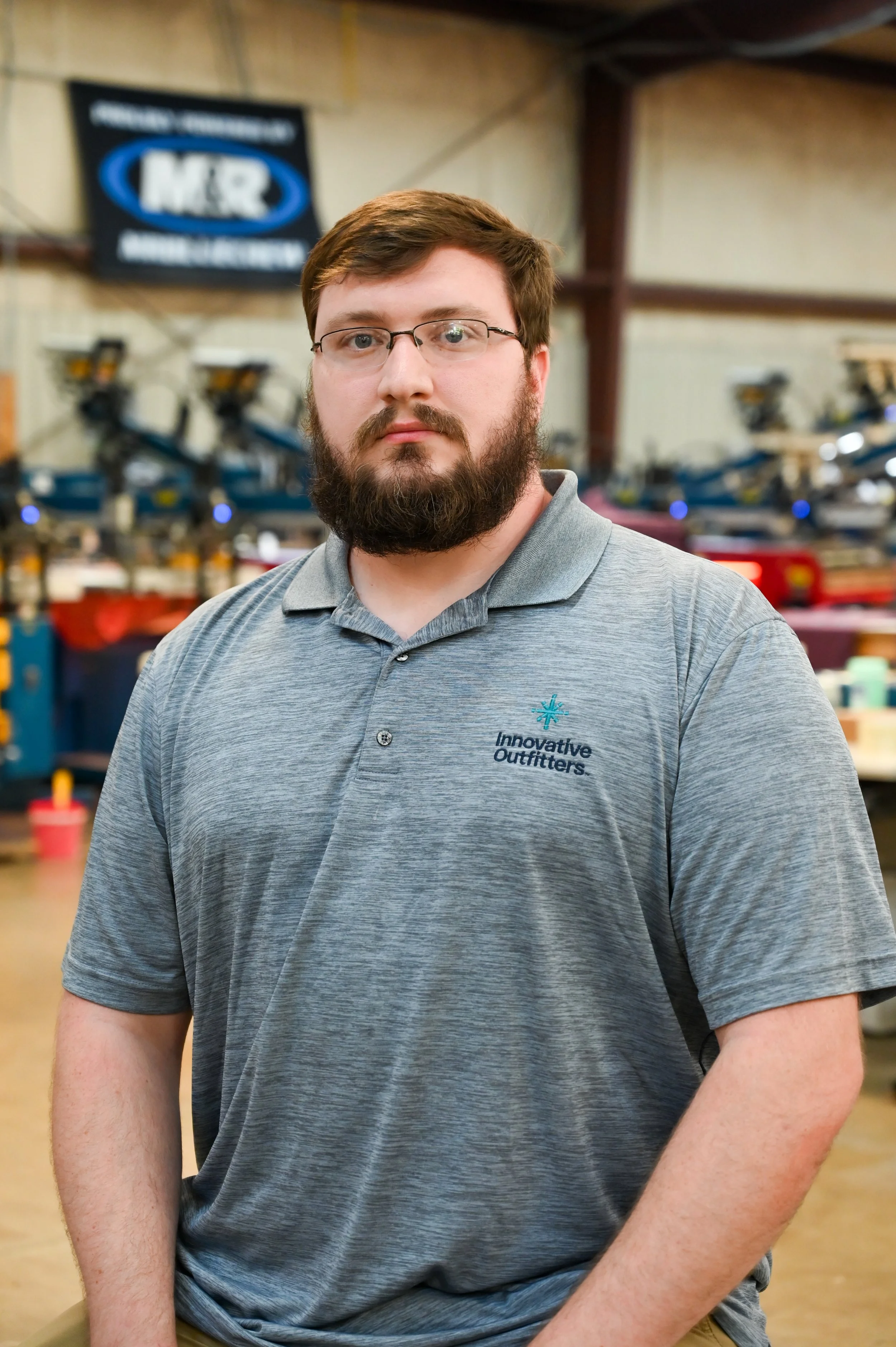 A man with glasses and a beard, wearing a gray polo shirt with the logo 'Innovative Outfitters,' standing inside a marine or outdoor equipment store.
