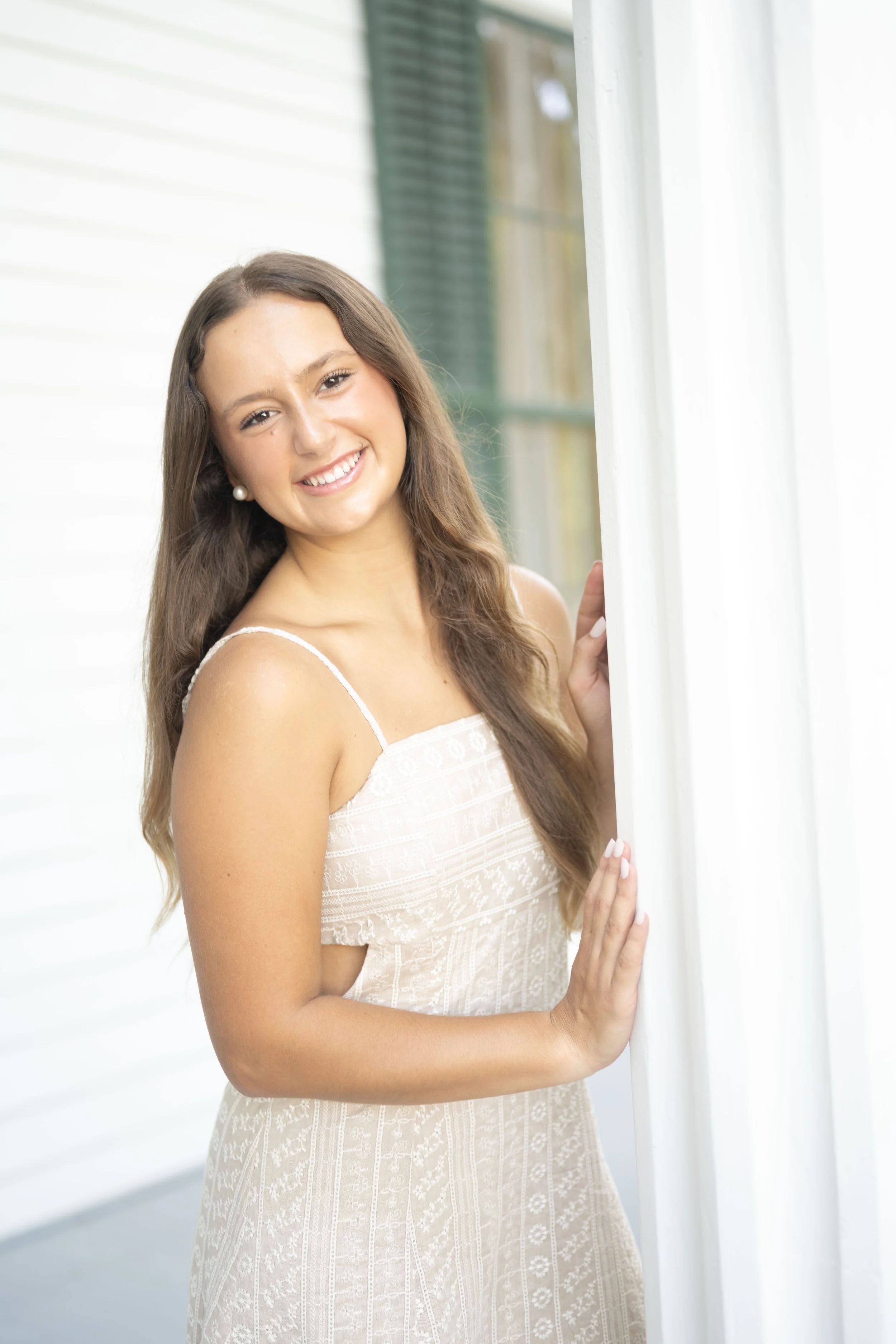 Woman in a light-colored dress standing next to a white column, smiling.
