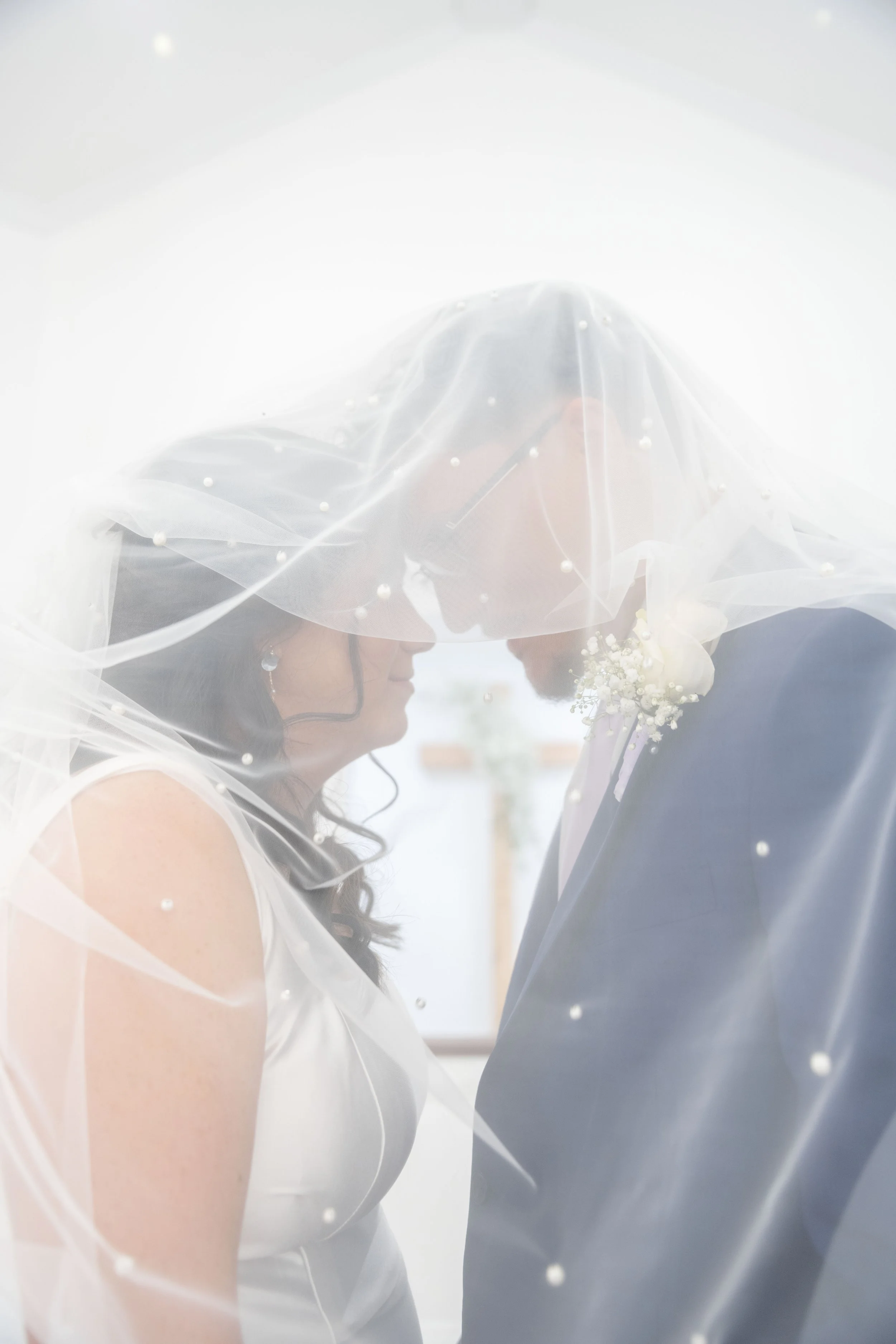 A bride and groom touching foreheads under a sheer veil during their wedding ceremony.