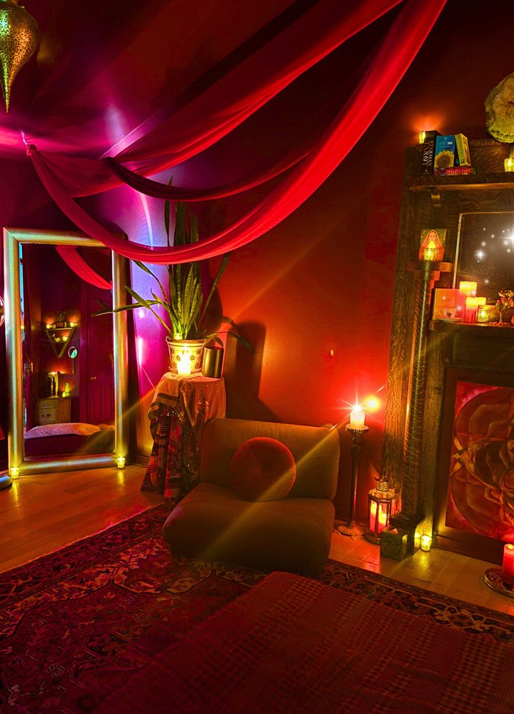 A cozy, dimly lit room with red and purple curtains, candles, and decorative items creating a warm ambiance at Joytown, a transformational retreat & tantra sanctuary in Colorado.
